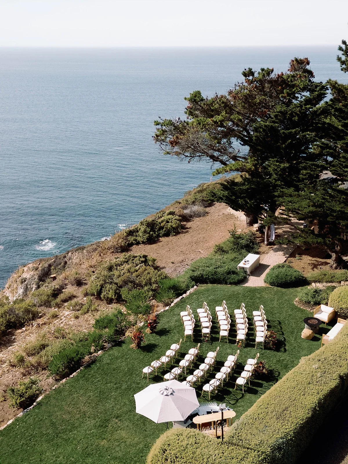 Aerial view of intimate wedding ceremony on coastal cliffside lawn overlooking the Pacific Ocean, Big Sur wedding photographer California