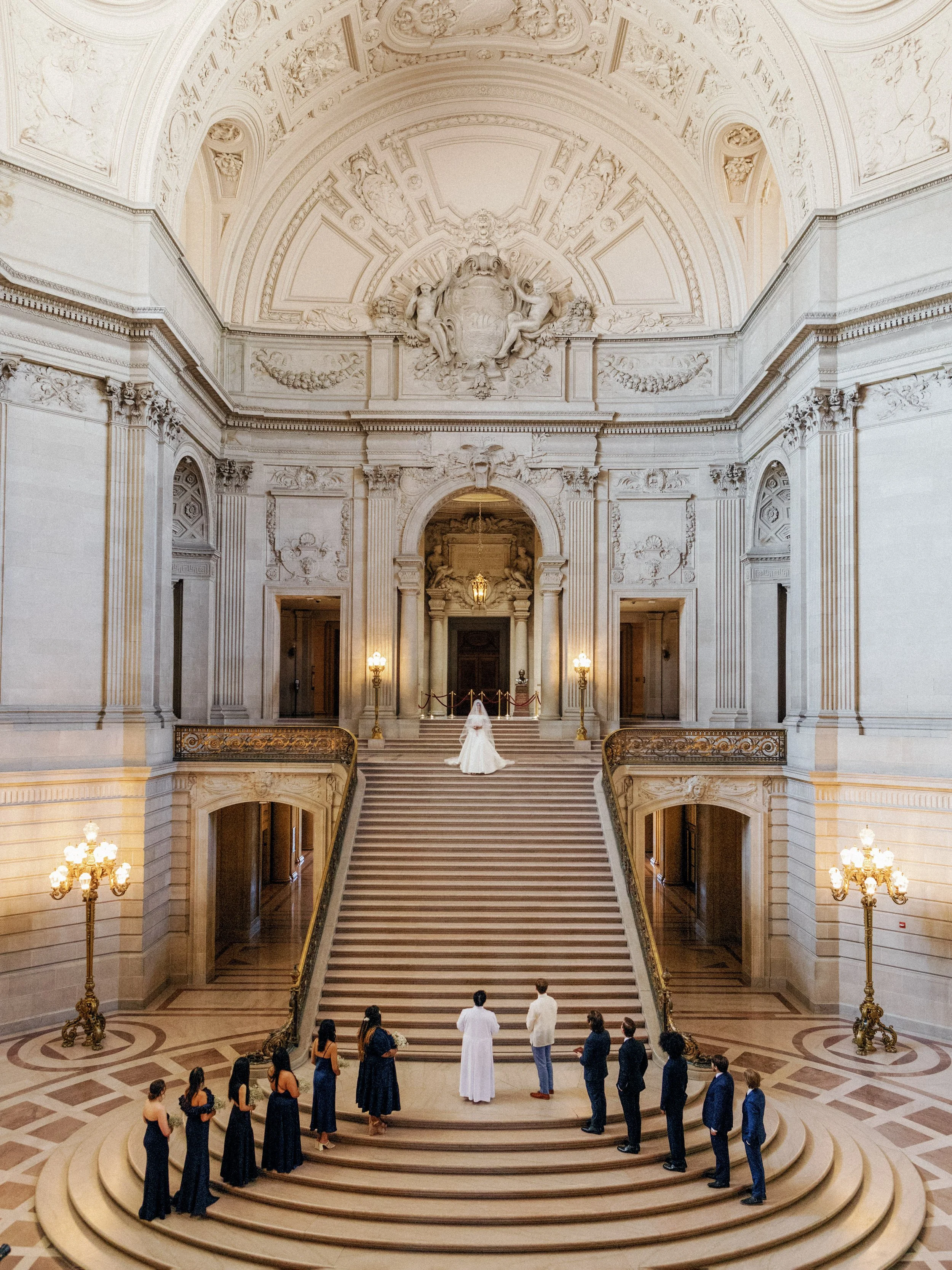 Wedding ceremony on the grand staircase at San Francisco City Hall viewed from above — bride at the top, wedding party gathered below, film photography by Radostina Boseva