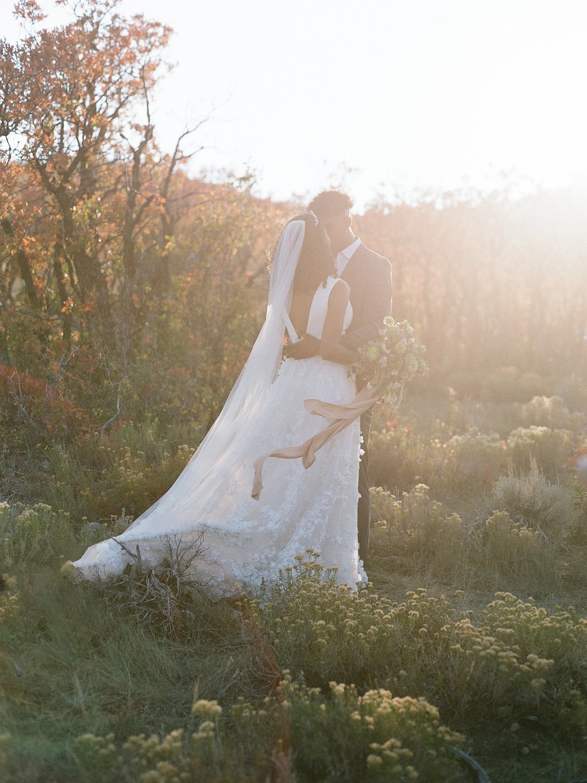 Bride and groom embracing in wildflower meadow at golden hour, wedding portrait photographed on film in Mendocino