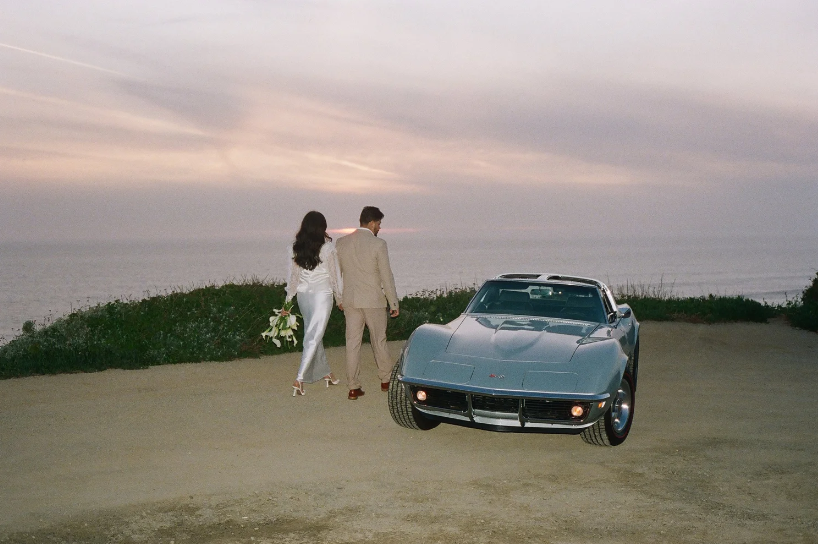 bride and groom walking toward the pacific ocean at dusk beside a vintage corvette, big sur california — film elopement photography by Radostina Boseva