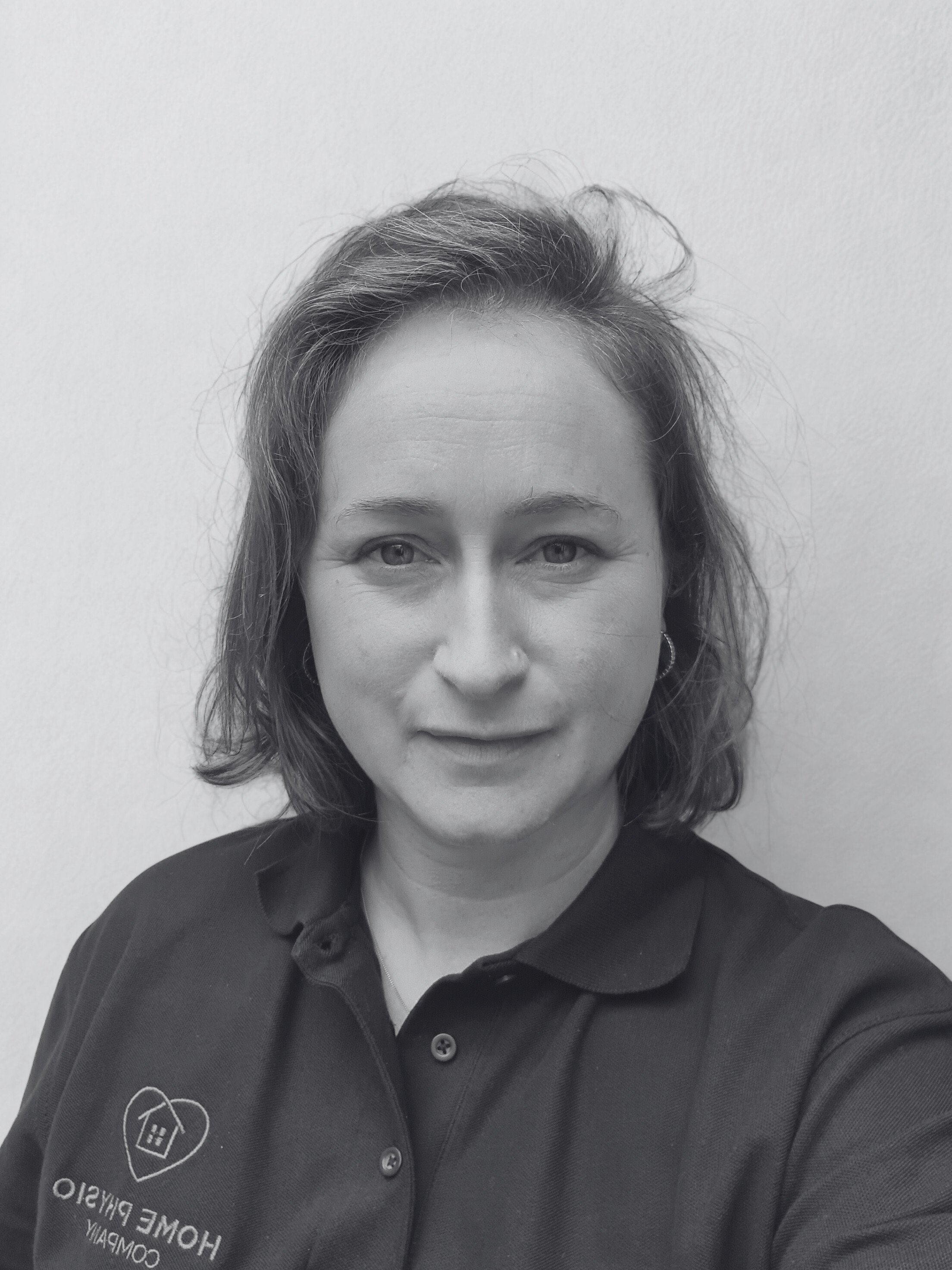 Black and white photo of woman smiling gently wearing dark polo with home physio company logo