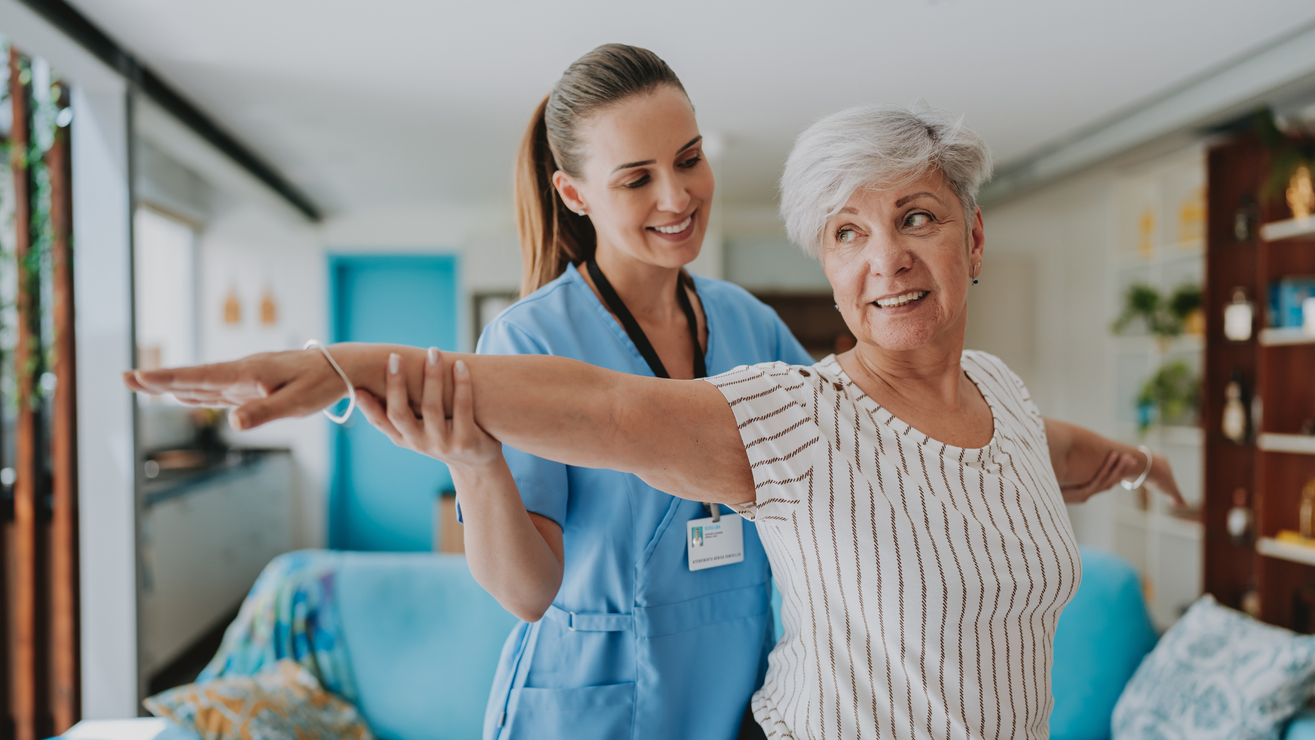 A healthcare worker assisting an elderly woman with arm stretches in a bright room.