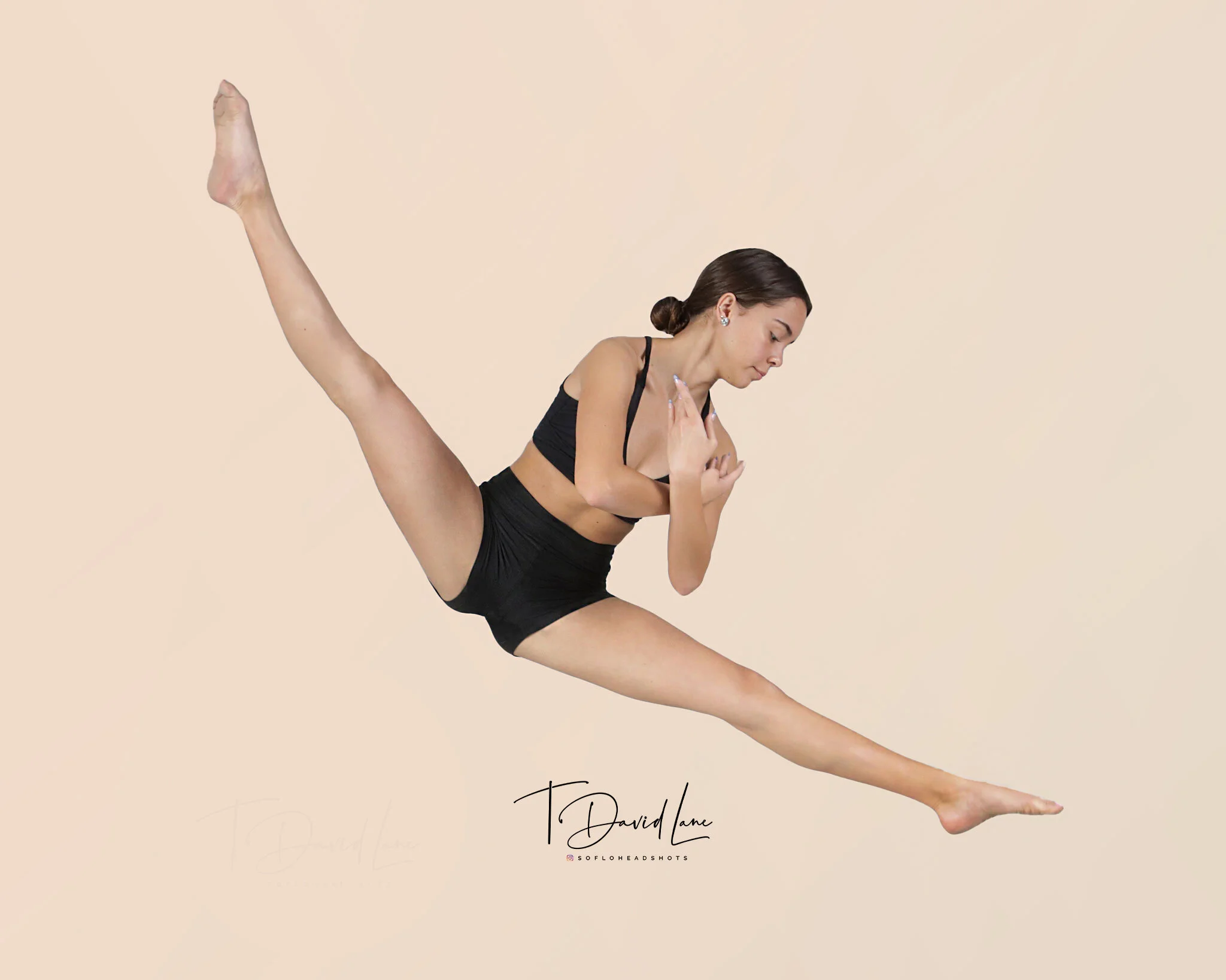 Professional dance portrait of a female dancer performing a dramatic split leap against a beige studio background.