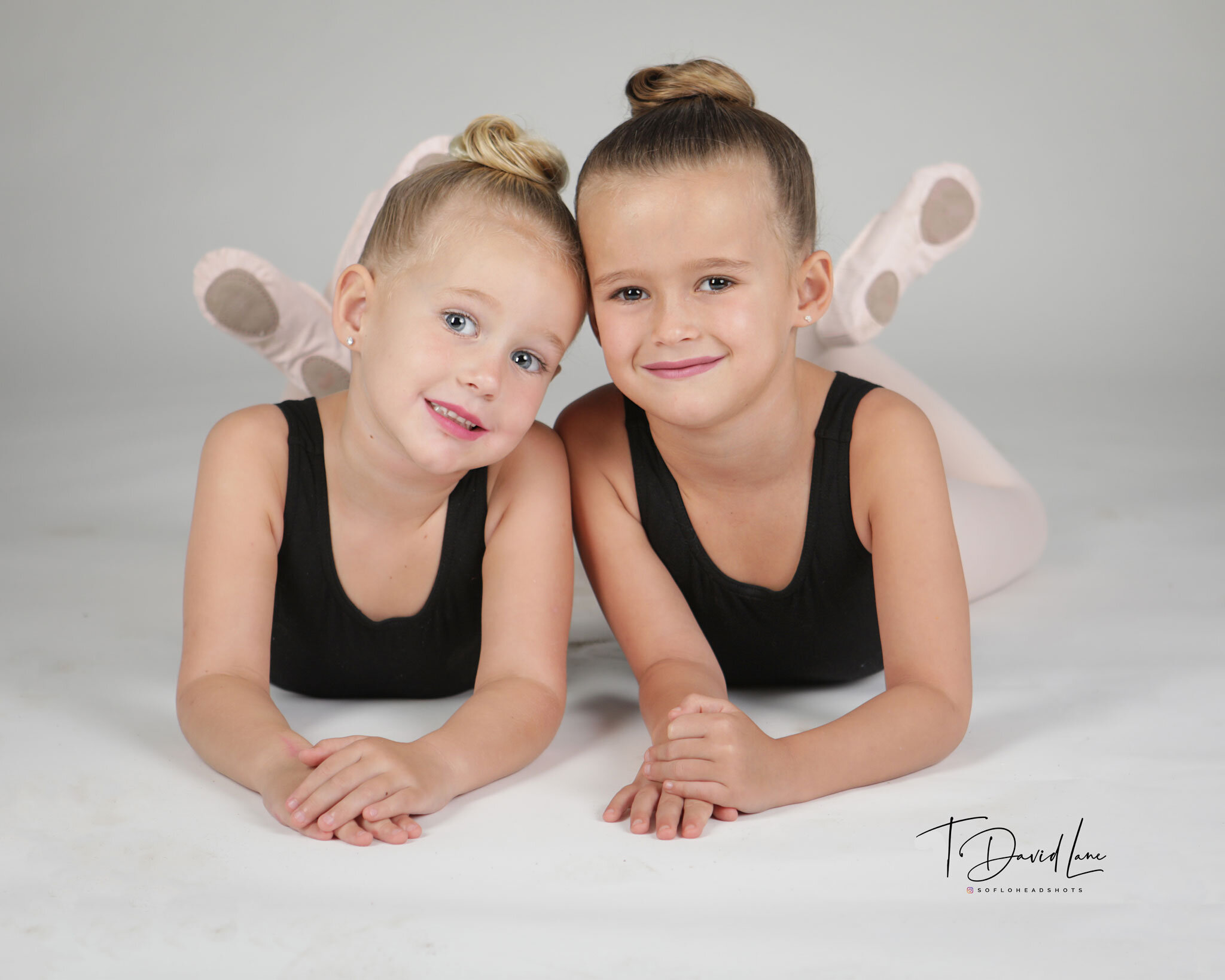 Studio portrait of two young dancers wearing black dance outfits and smiling together against a light gray background.
