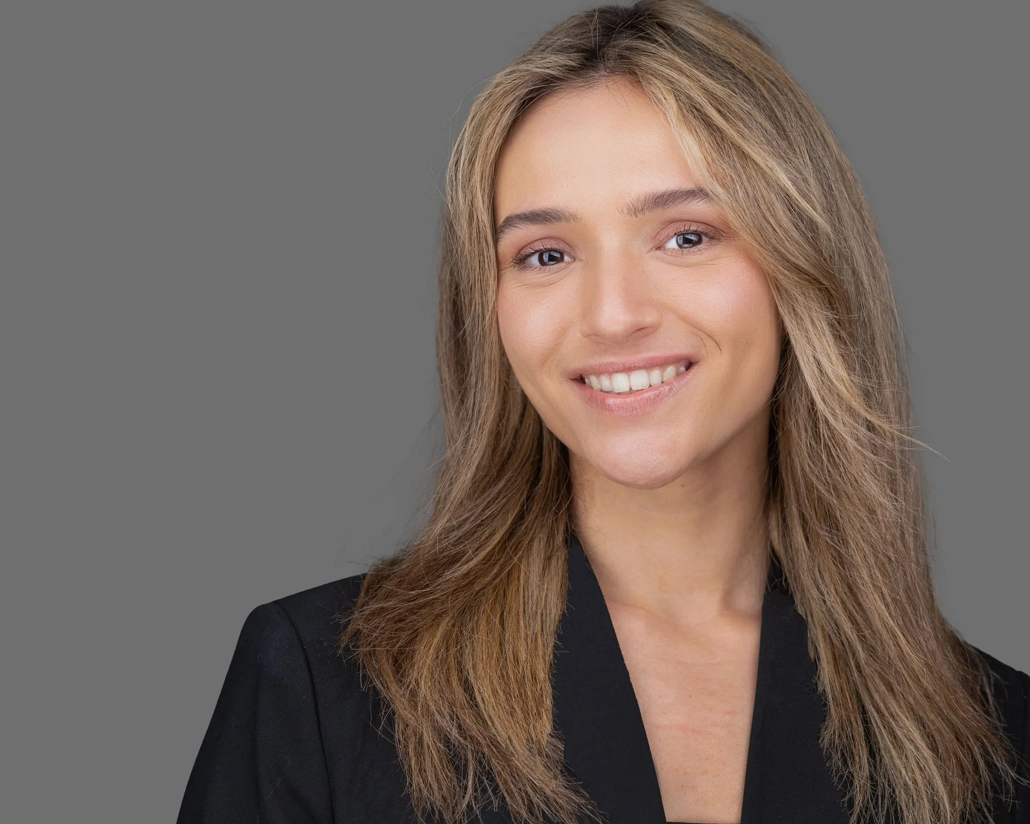 Professional female business portrait featuring a black blazer, natural smile, and neutral gray background.