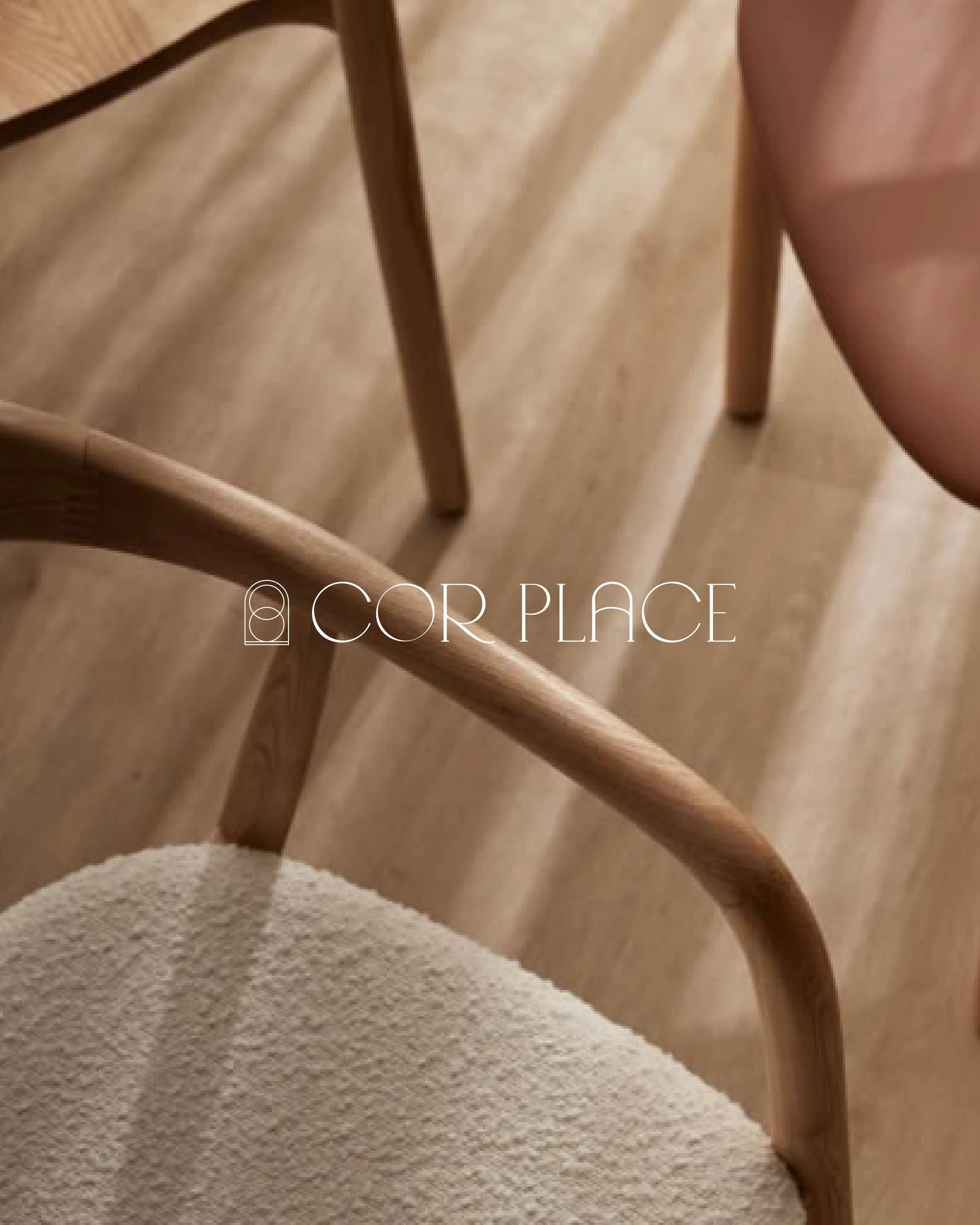 Close-up of a wooden chair with a light-colored cushion, set on a wooden floor. The photo includes a partial view of a person's knee and the text 'COR PLACE' overlaid.