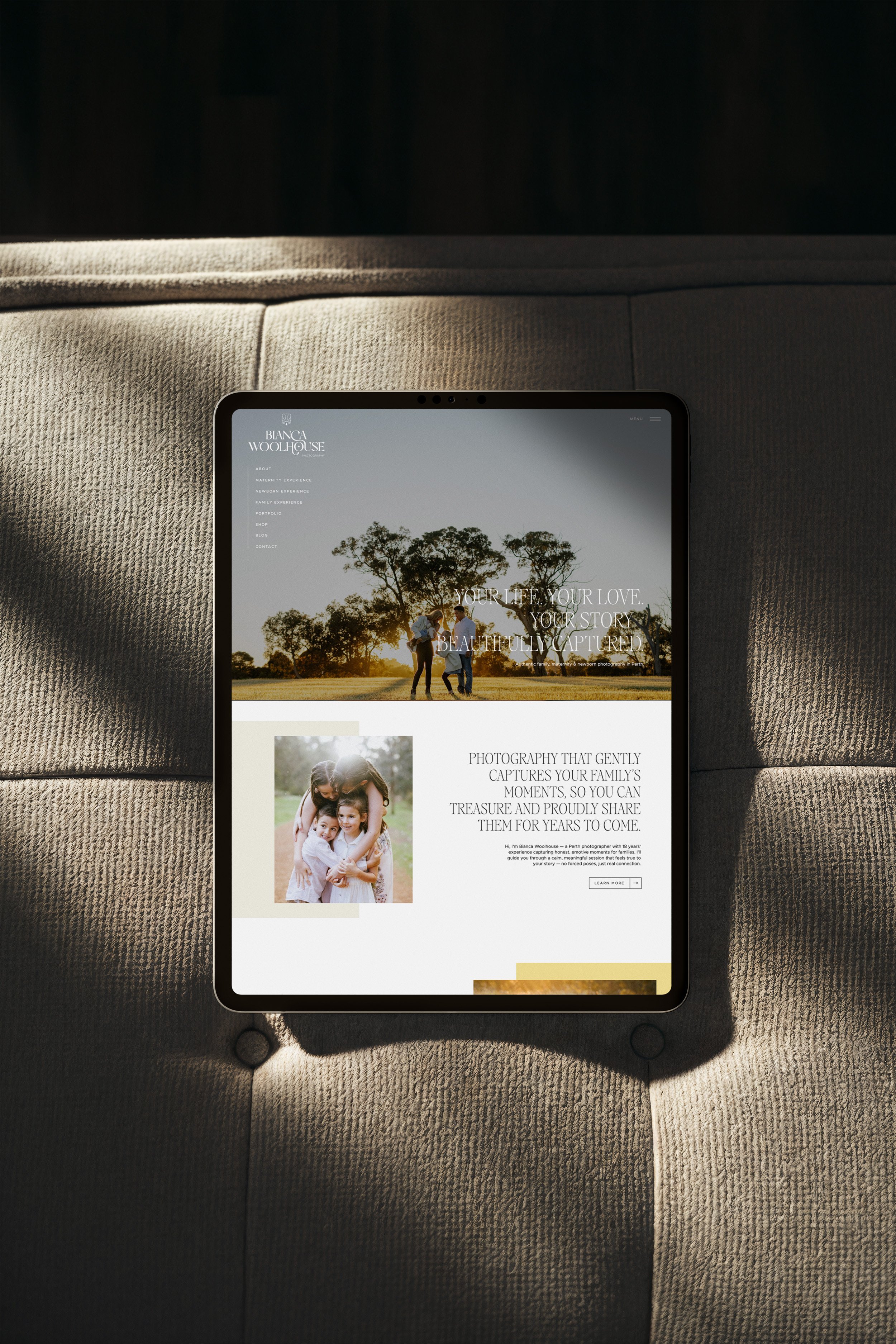 An iPad displaying a photography website resting on a textured beige couch, with sunlight casting shadows around it.