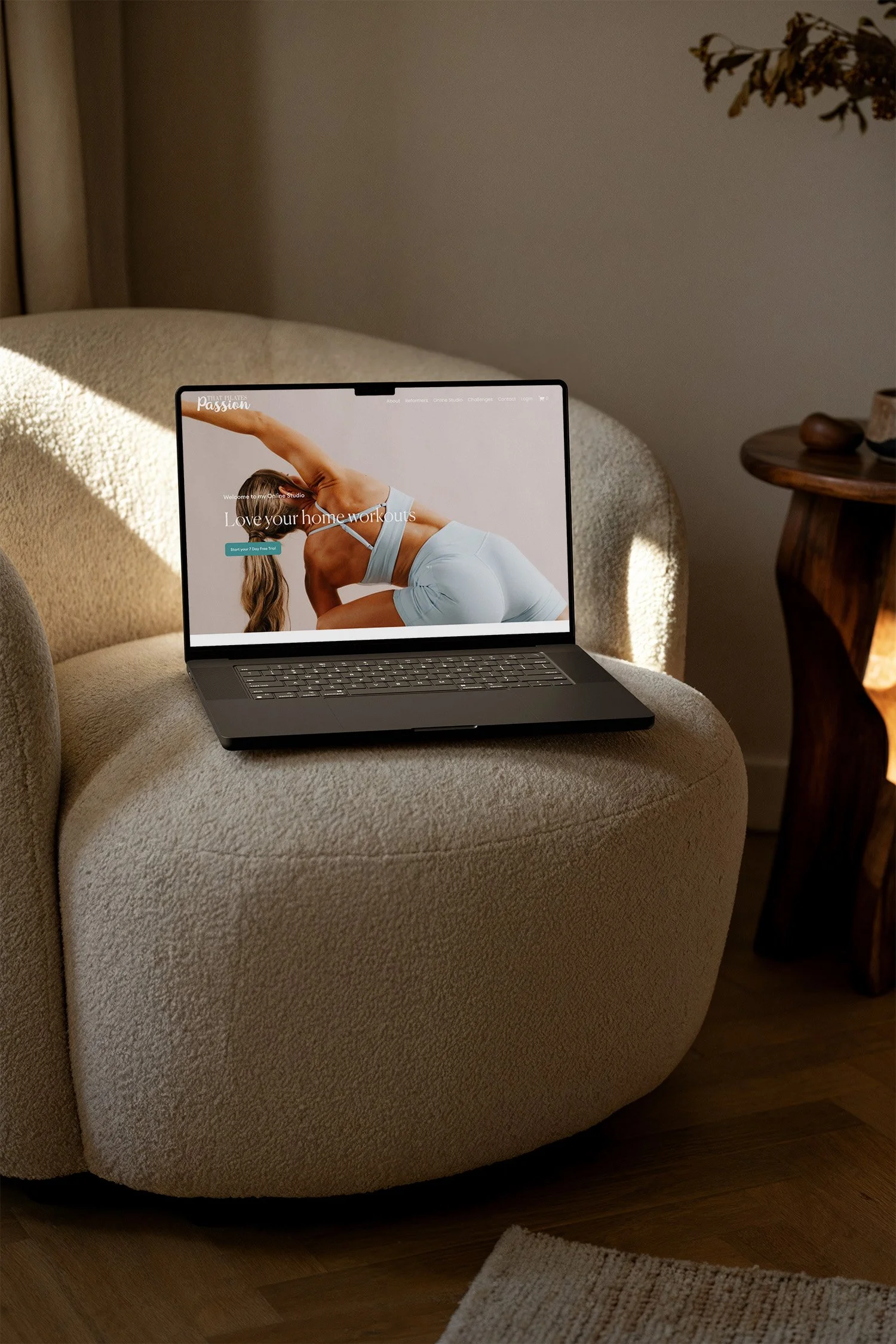 A laptop resting on a beige textured armchair in a cozy room, displaying a fitness website with a woman in workout attire performing a yoga pose.