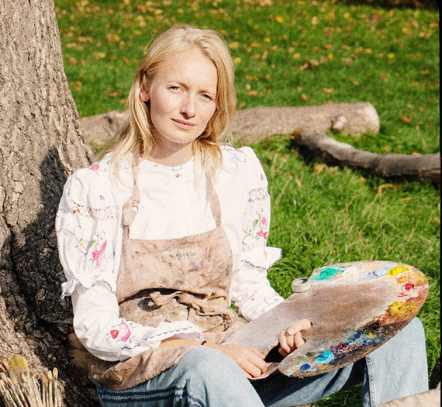 British painter Emily Peers seated outdoors holding her palette.