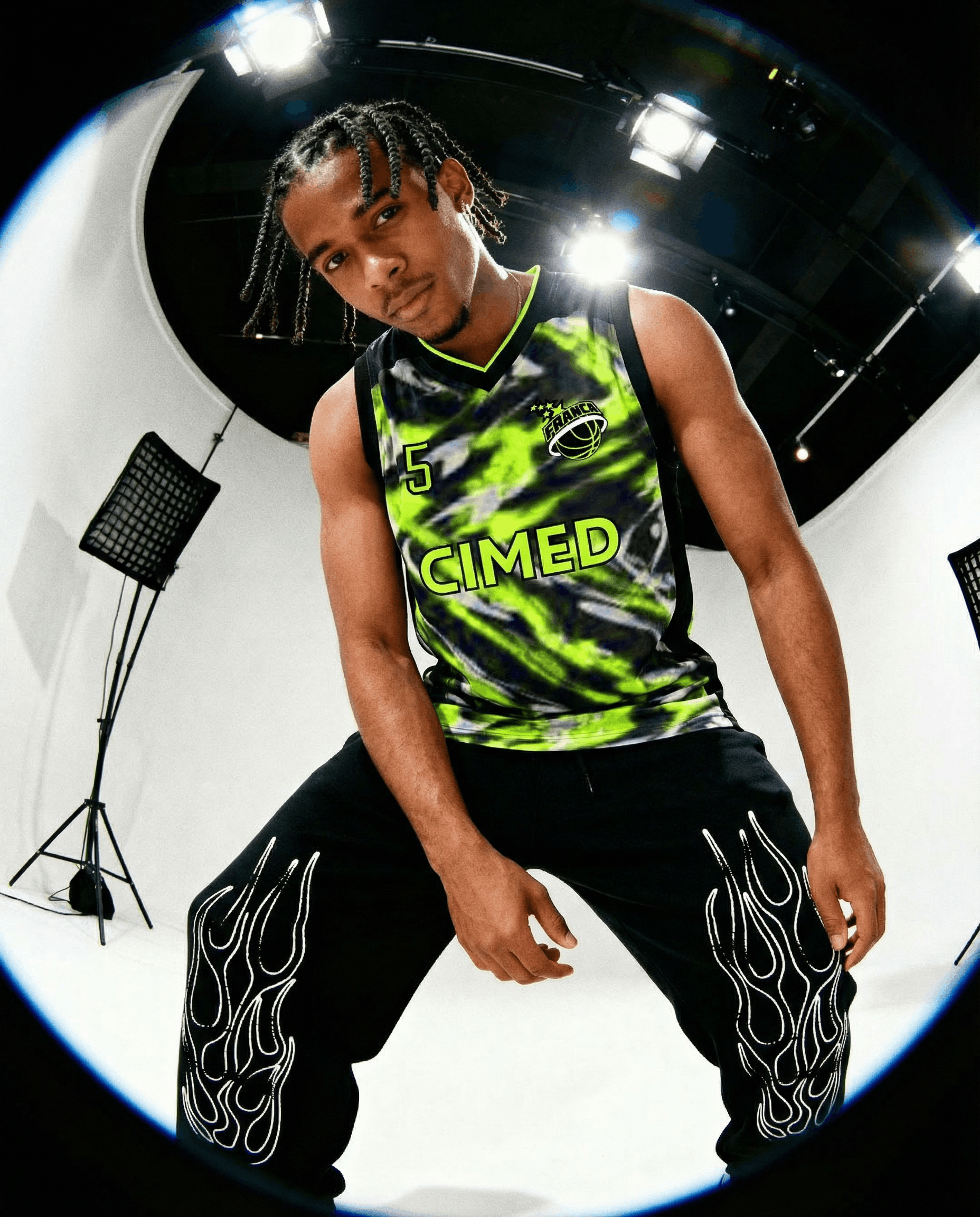 Ein männlicher Basketballspieler in einem schwarzen und grünen Trikot, der in einem Fotostudio poseiert.