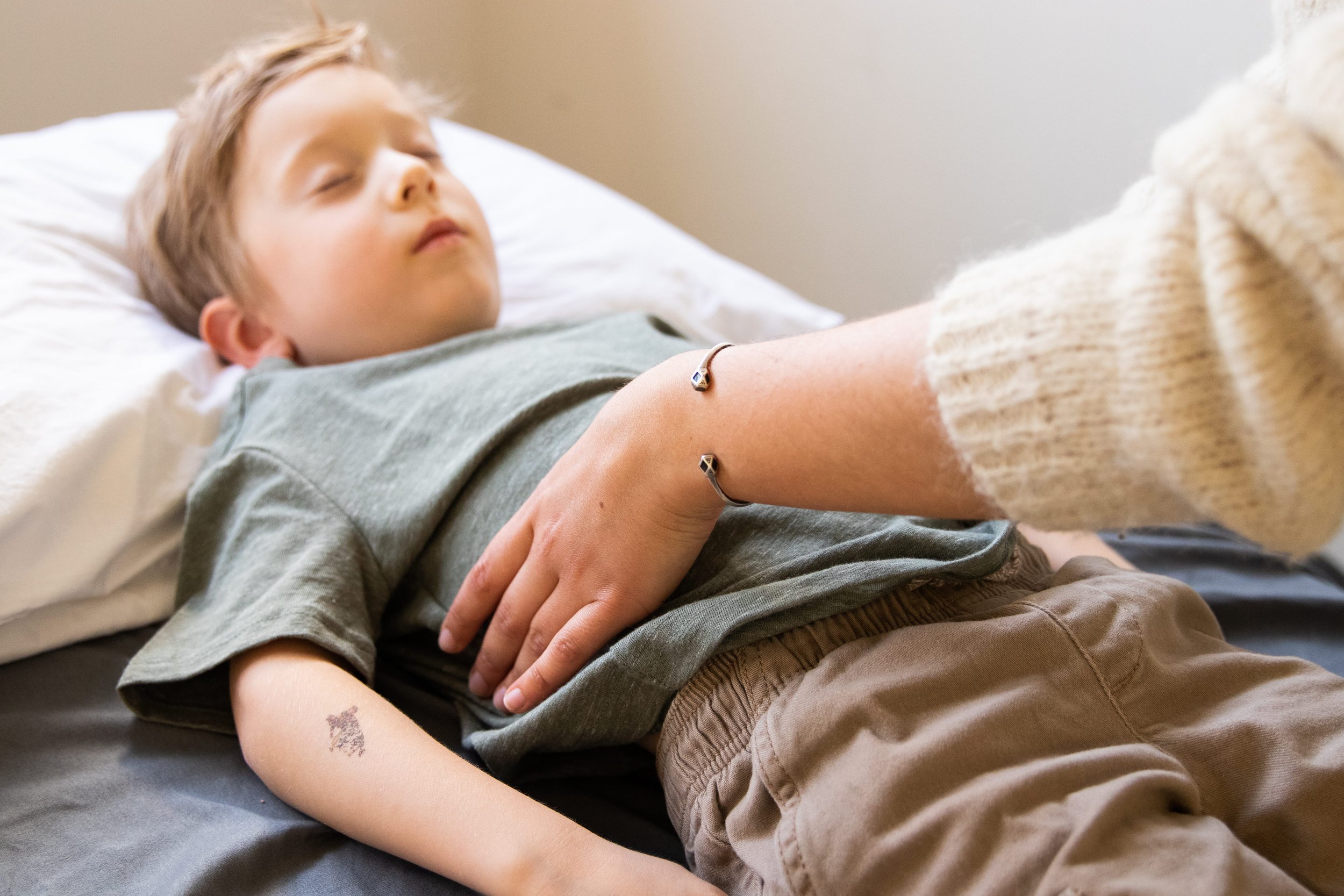 A woman with curly brown hair wearing a polka dot blouse holds a person's arm while checking their pulse in a clinical setting.