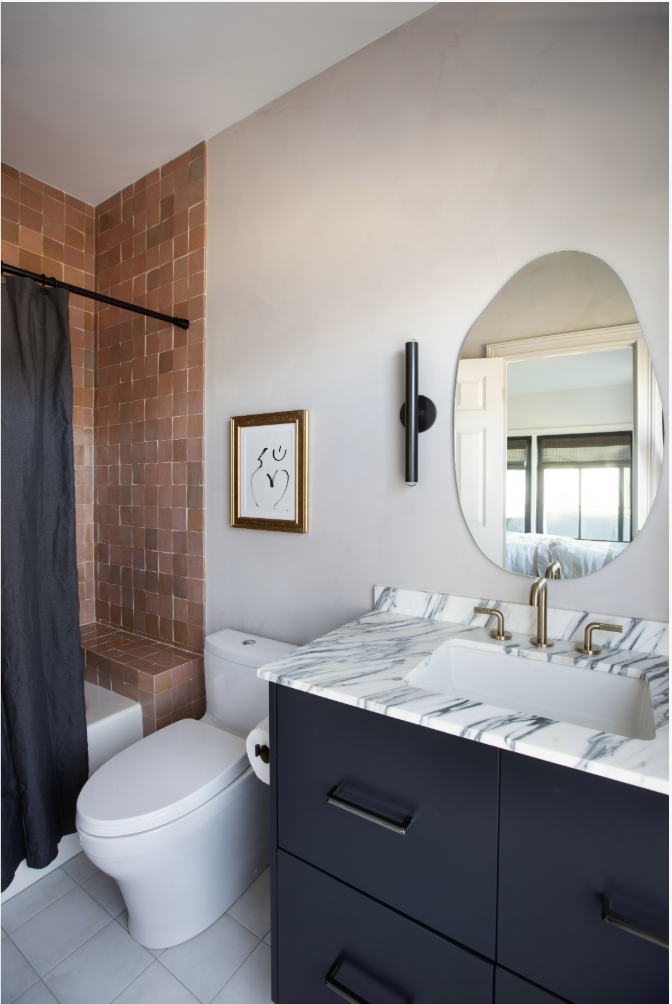 Modern bathroom with black vanity, marble countertop, oval mirror, white toilet, and walk-in shower with pink tiles and black curtain