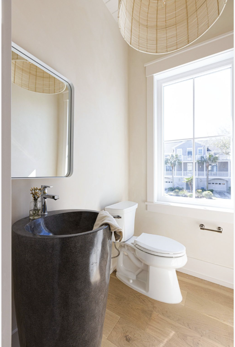 Bathroom with a black stone sink, a white toilet, a large window, a wall-mounted mirror, and a paper lantern ceiling light.