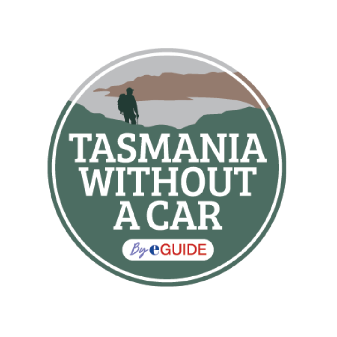 A couple holding hands walking on a rocky coastal path with mountains and ocean in the background under partly cloudy skies.