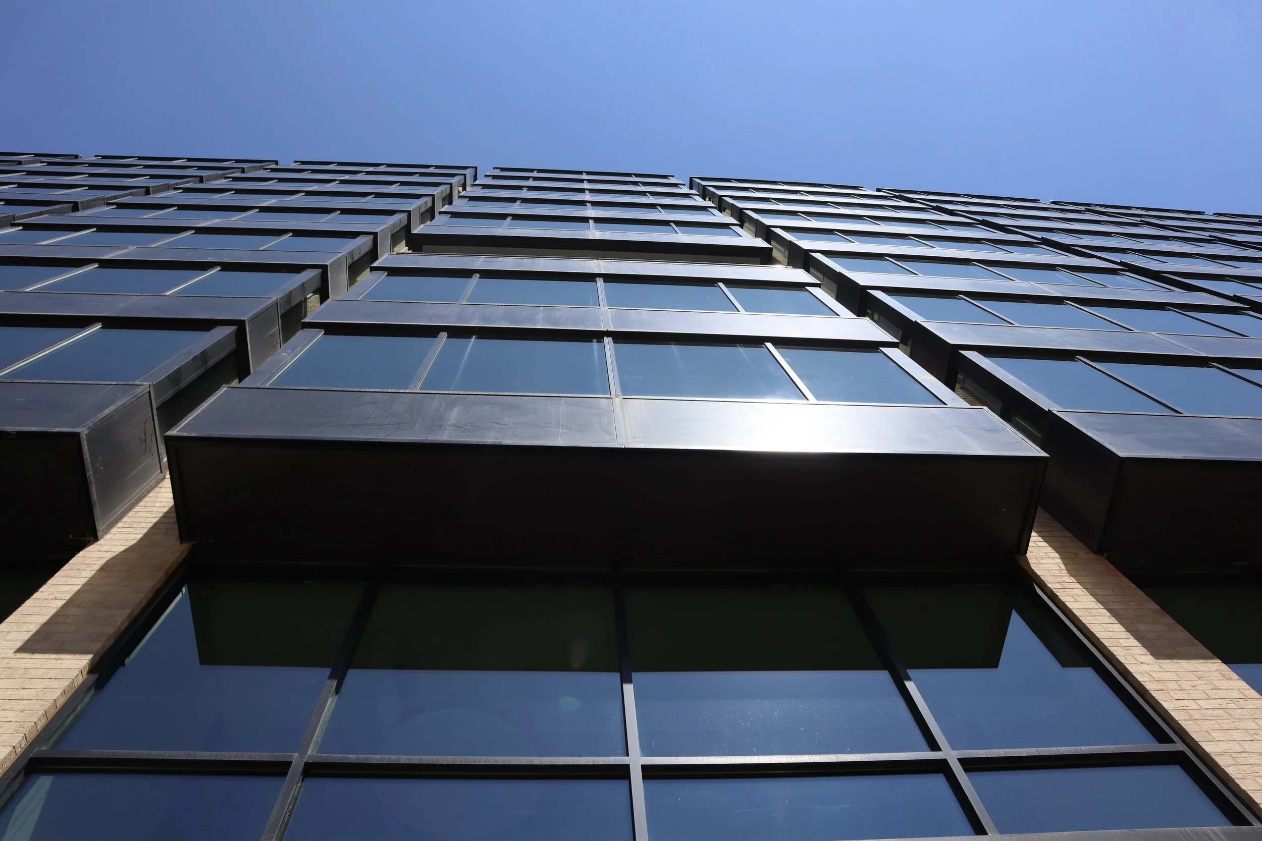 Looking up at a modern glass skyscraper against a blue sky.