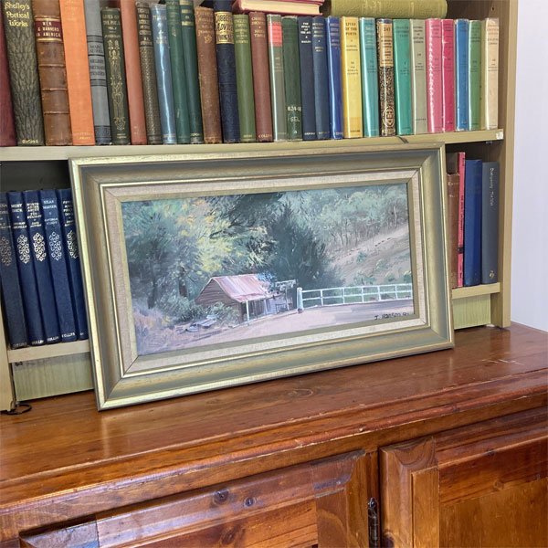 John Hansen (1989) painting Raspberry Creek shed, framed rural scene with red tin roof, white fence, and creek-side bushland.