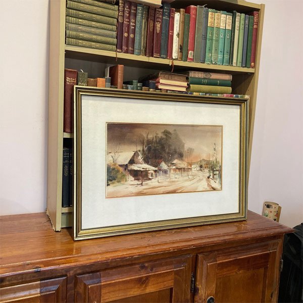 Lionel Tapsell sofala scene in muted watercolor. Framed artwork shown in cozy interior with bookshelf backdrop.