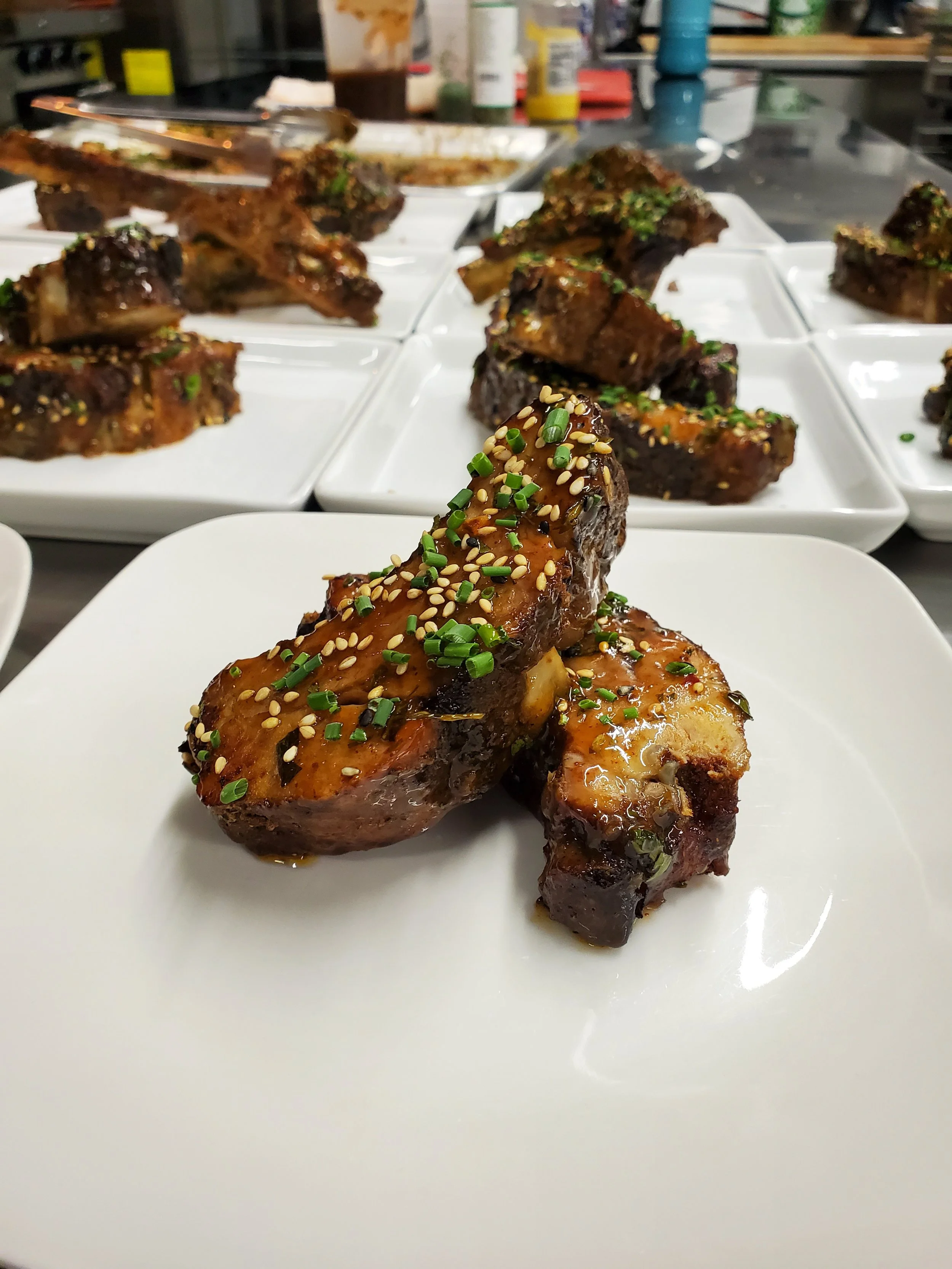 Glazed pork baby back ribs garnished with scallion and sesame seeds, served as part of the Lone Peak Provisions catering menu in Bozeman, Montana.