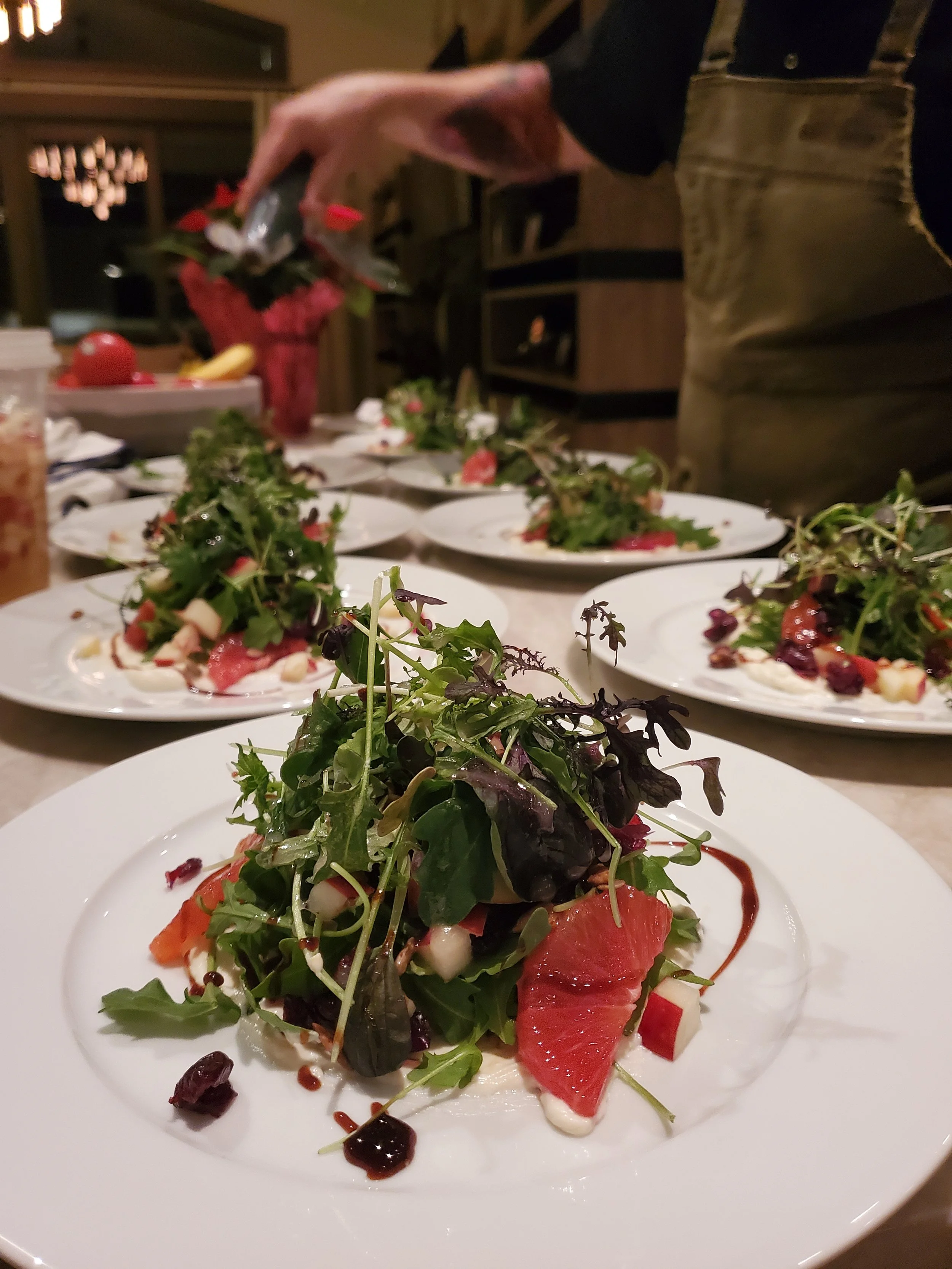 A plated salad with mixed greens, slices of radish, tomato, and dressing, set on a dinner table.