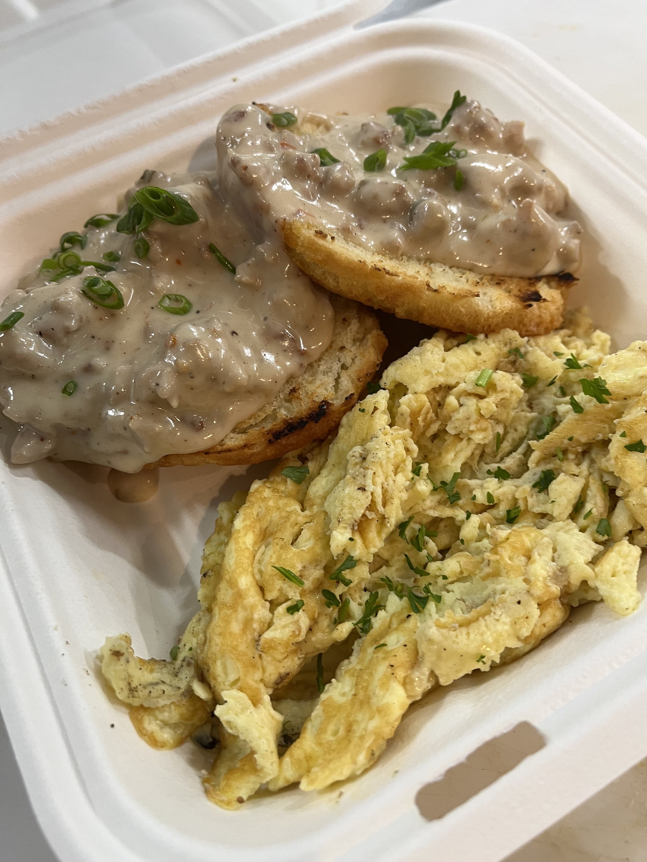 Breakfast plate with scrambled eggs, a biscuit with sausage gravy topped with chopped green onions. Available at Lone Peak Povisions in Bozeman, Montana.