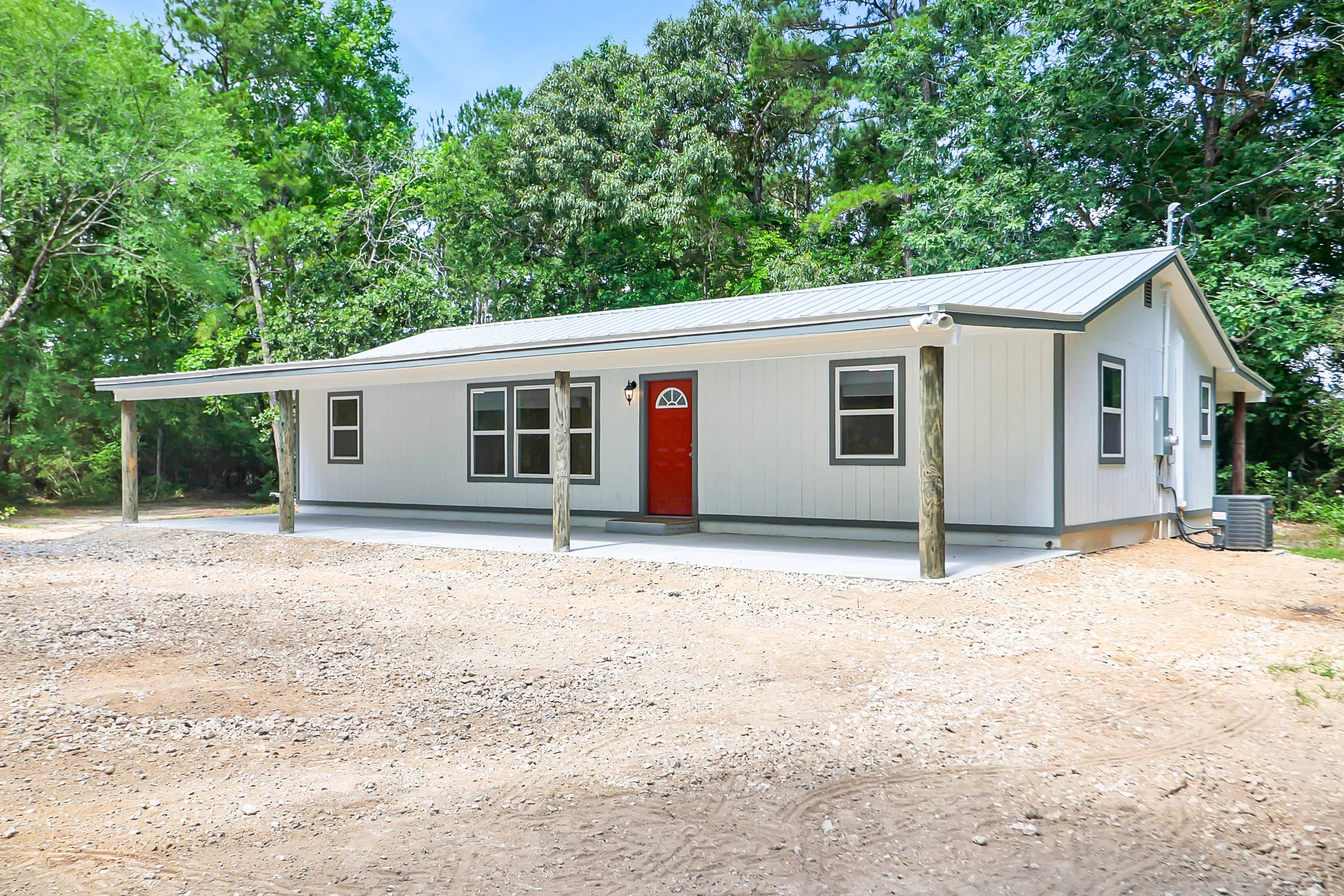 Small white house with a red door and covered porch surrounded by trees