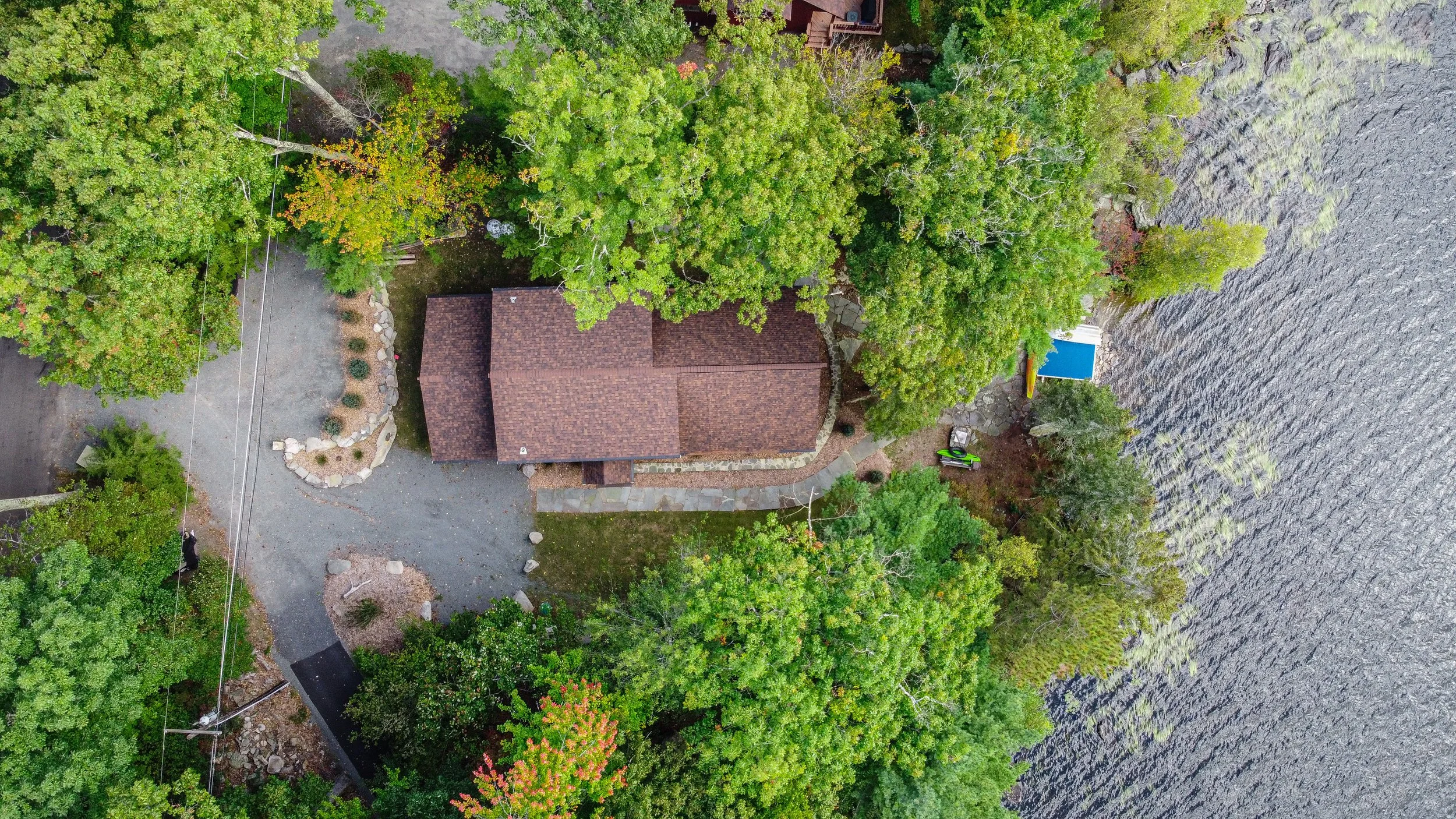 Aerial view of a house surrounded by trees near a body of water with a small dock.
