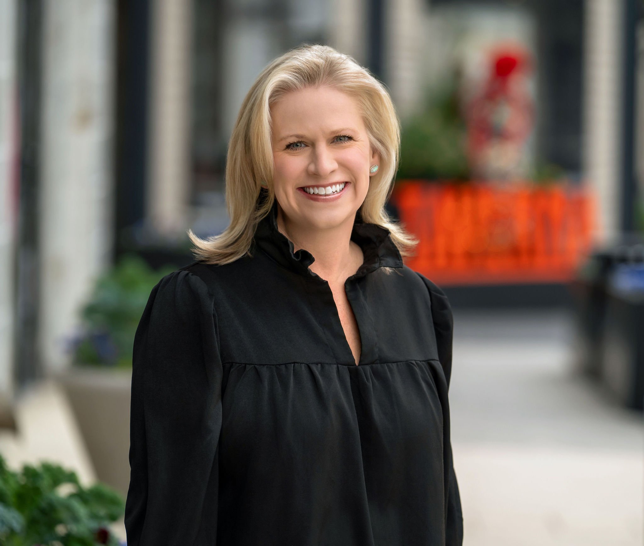 Licensed Professional Counselor, Dayna Kline,  smiling with blonde hair and wearing a light blue top with pink and green accents, standing outside her Dallas Texas counseling office.