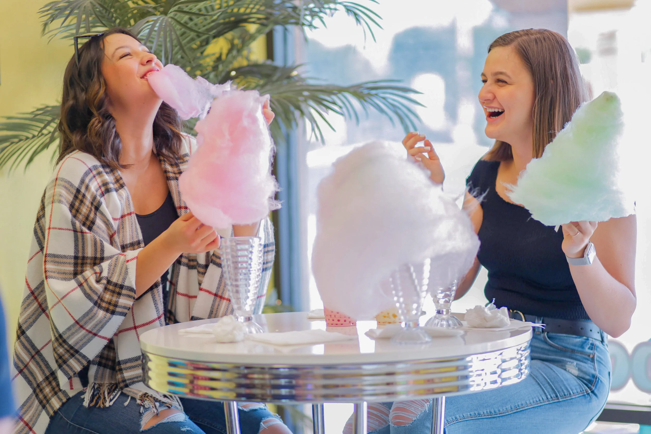 Two women eating cotton candy at a table and laughing