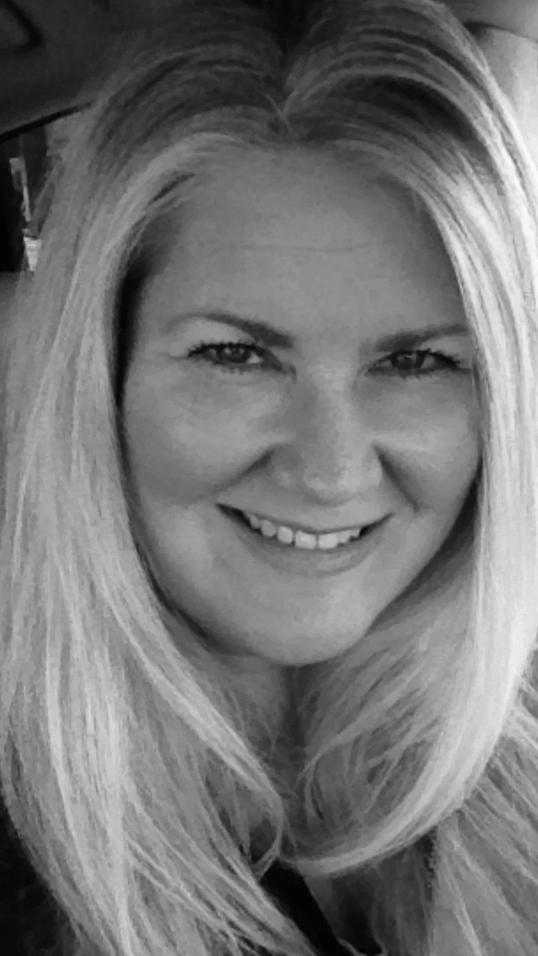 A woman with long, blonde hair smiling in black and white.