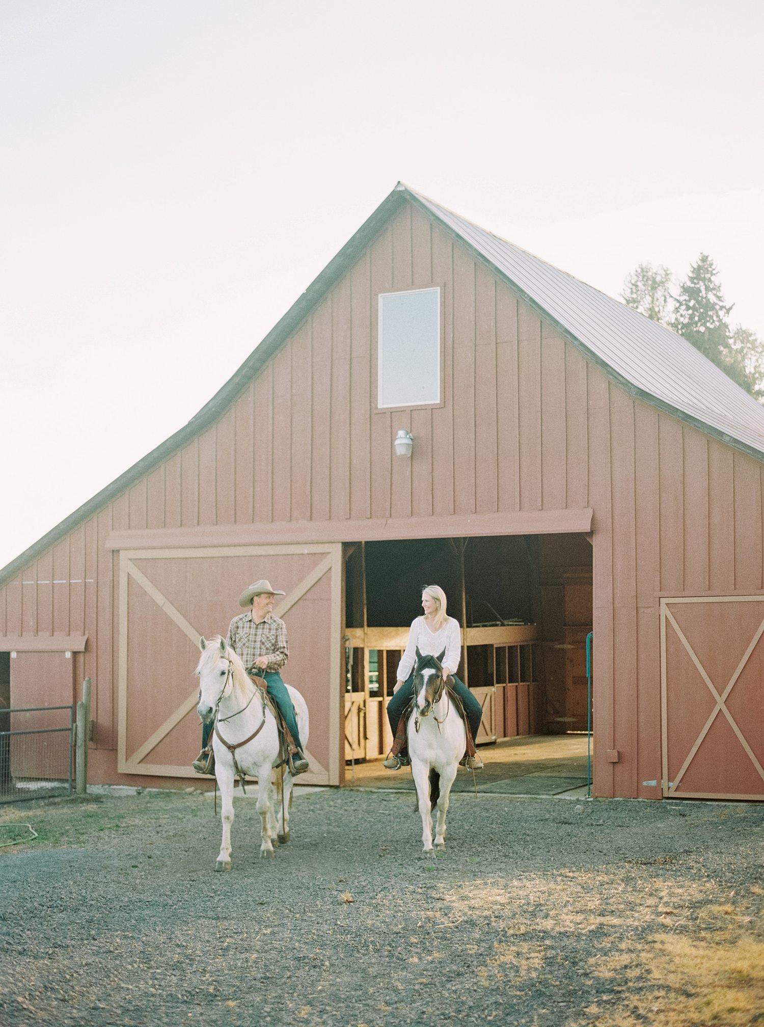 bride and groom riding horses out of barn