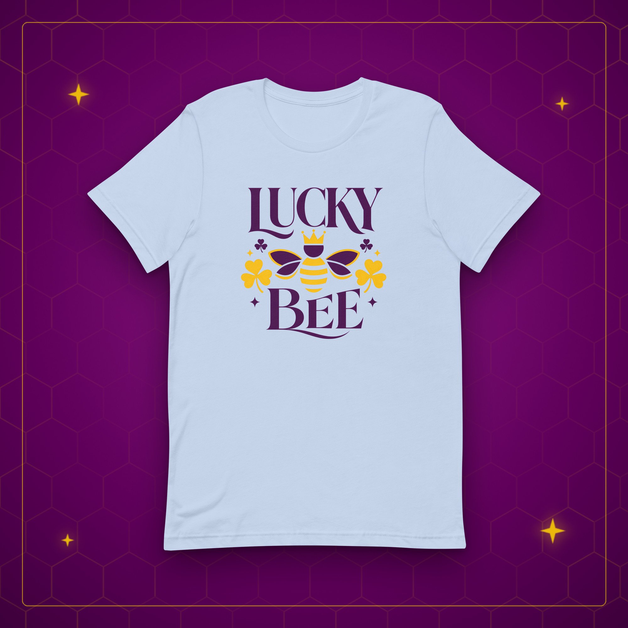 Lucky Bee tee in baby blue, laid flat on a purple background with gold sparkles