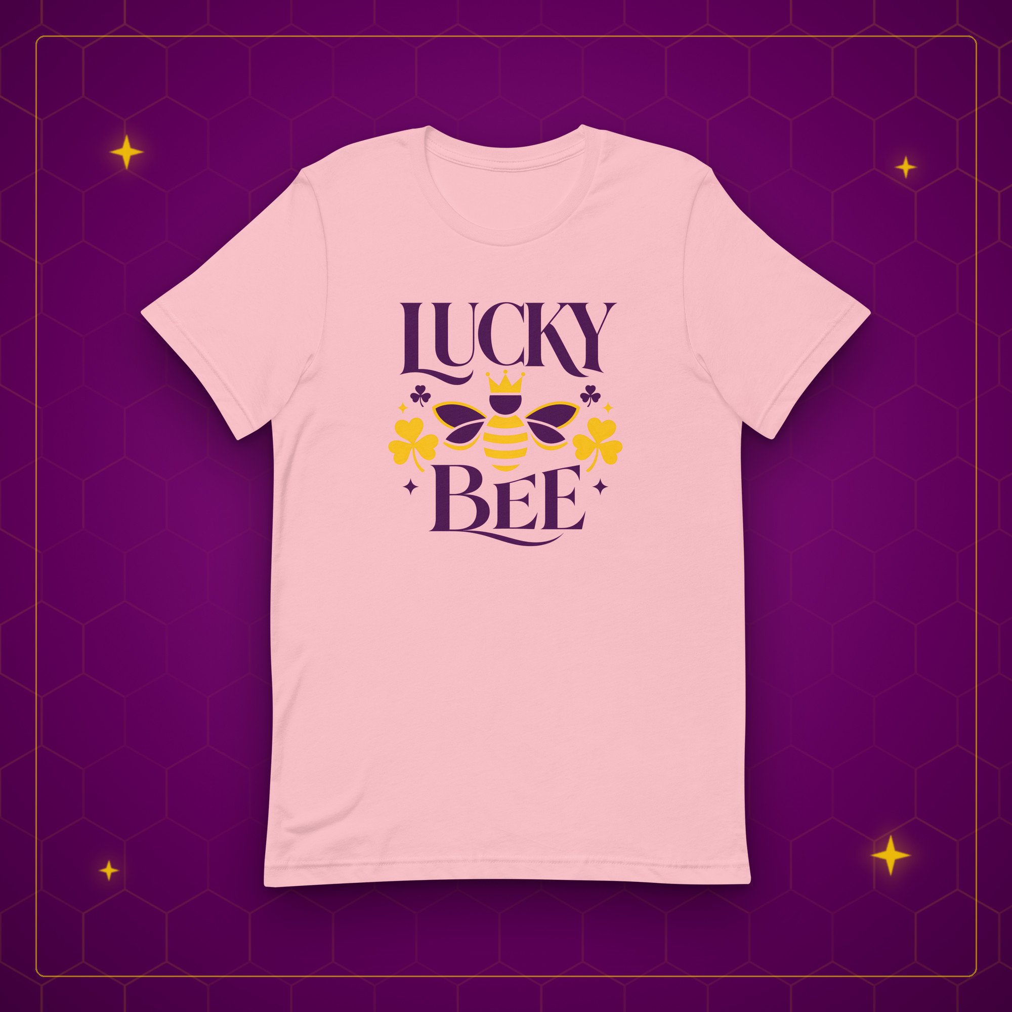 Lucky Bee tee in pink, laid flat on a purple background with gold sparkles