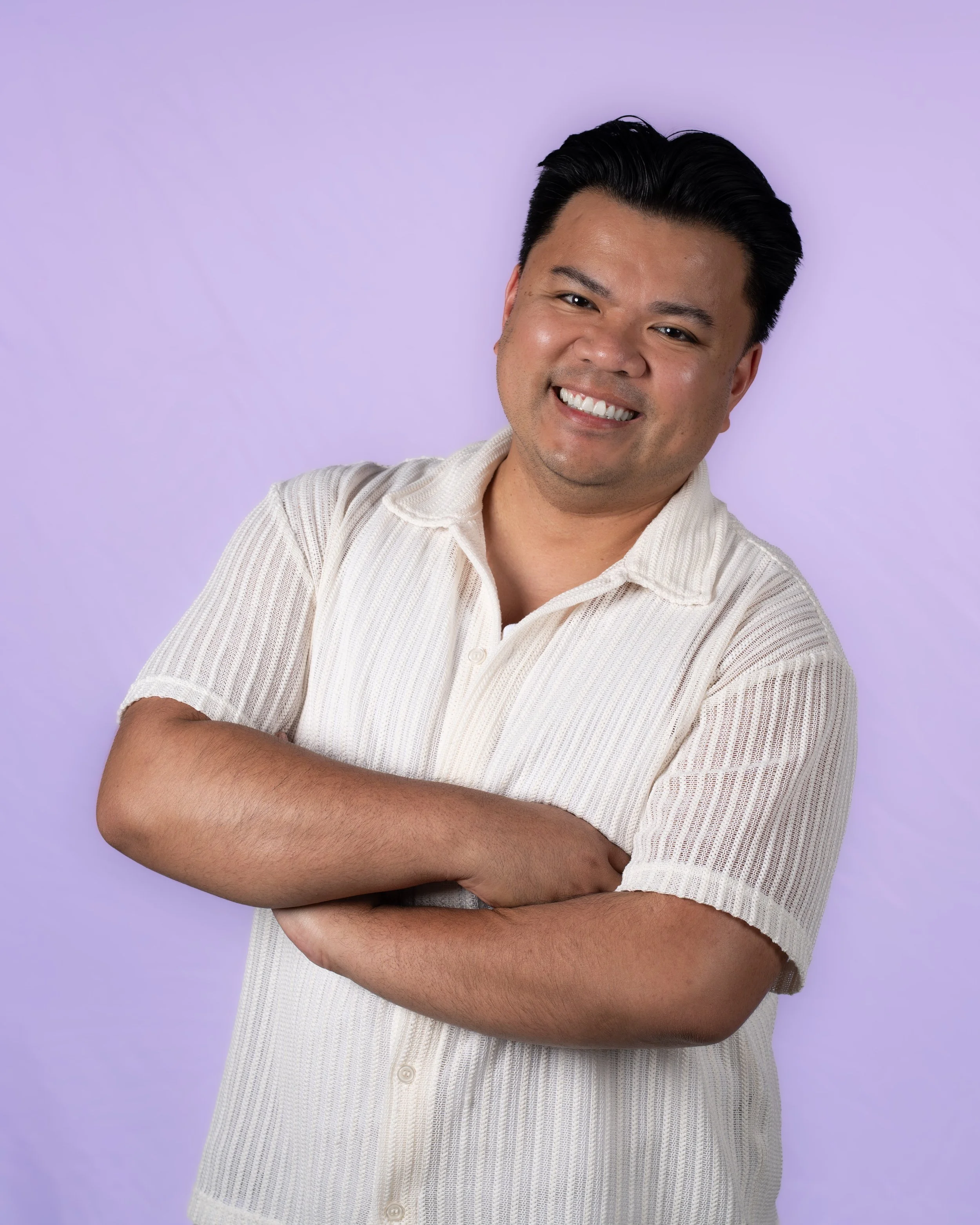 A man wearing a bright blue button-up shirt, with black, slicked-back hair, looking thoughtfully to the side, against a plain light-colored background.