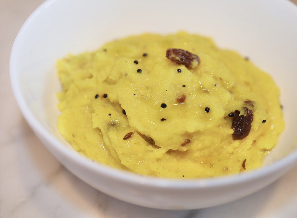 South Indian kesari dessert in a white bowl with raisins and black mustard seeds