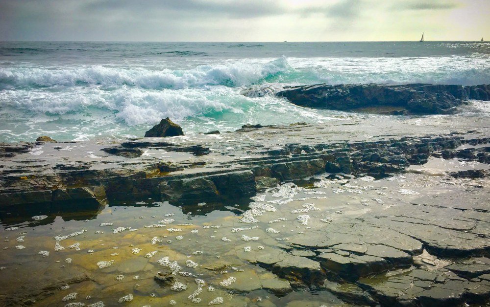 Rocky shoreline with ocean waves and distant sailboat