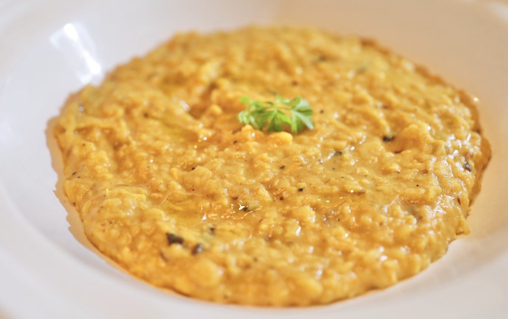 Creamy risotto garnished with a small green herb on top in a white dish.
