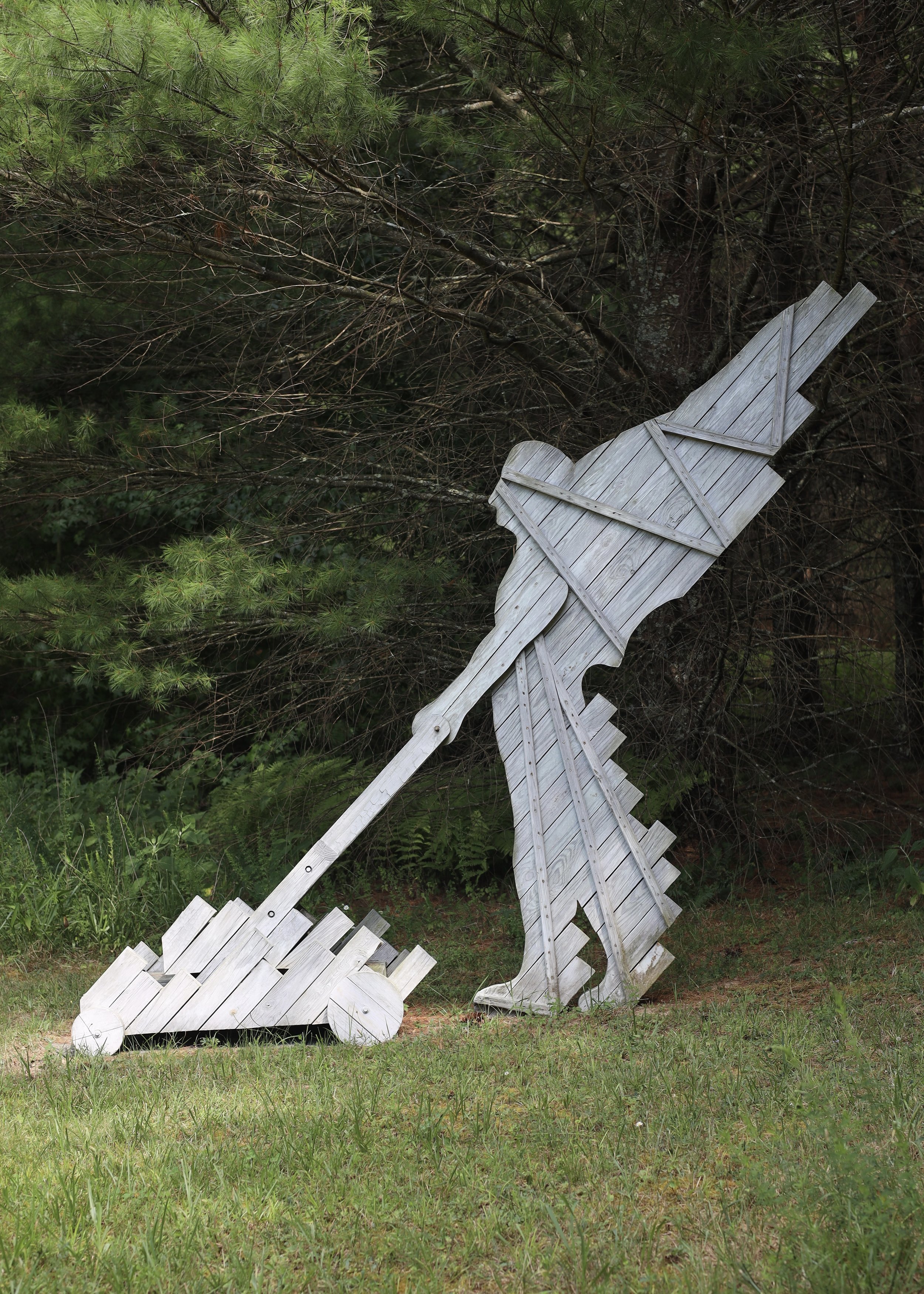 Wooden sculpture of a person with a lawn mower in a forest.