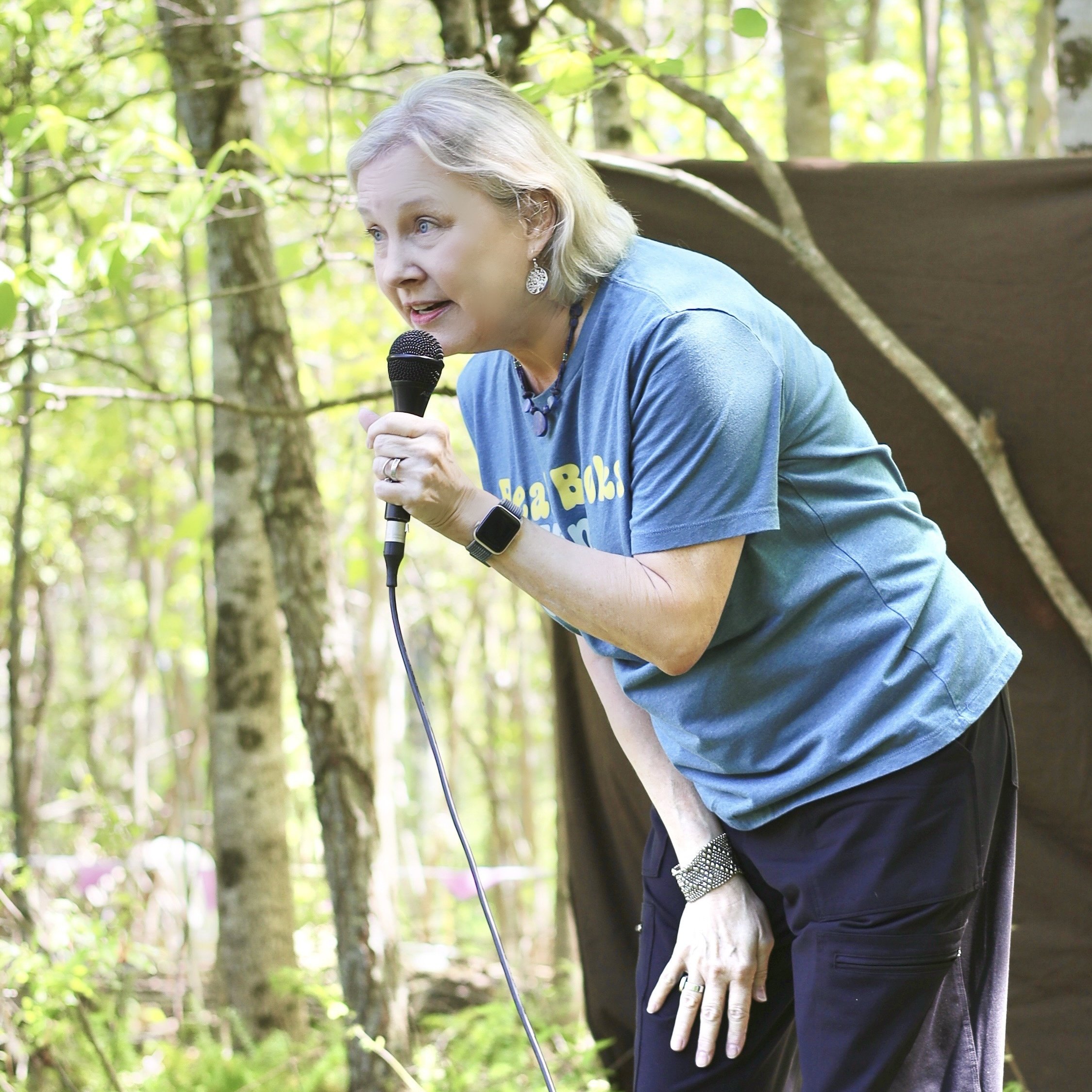 Woman speaking into a microphone outdoors among trees