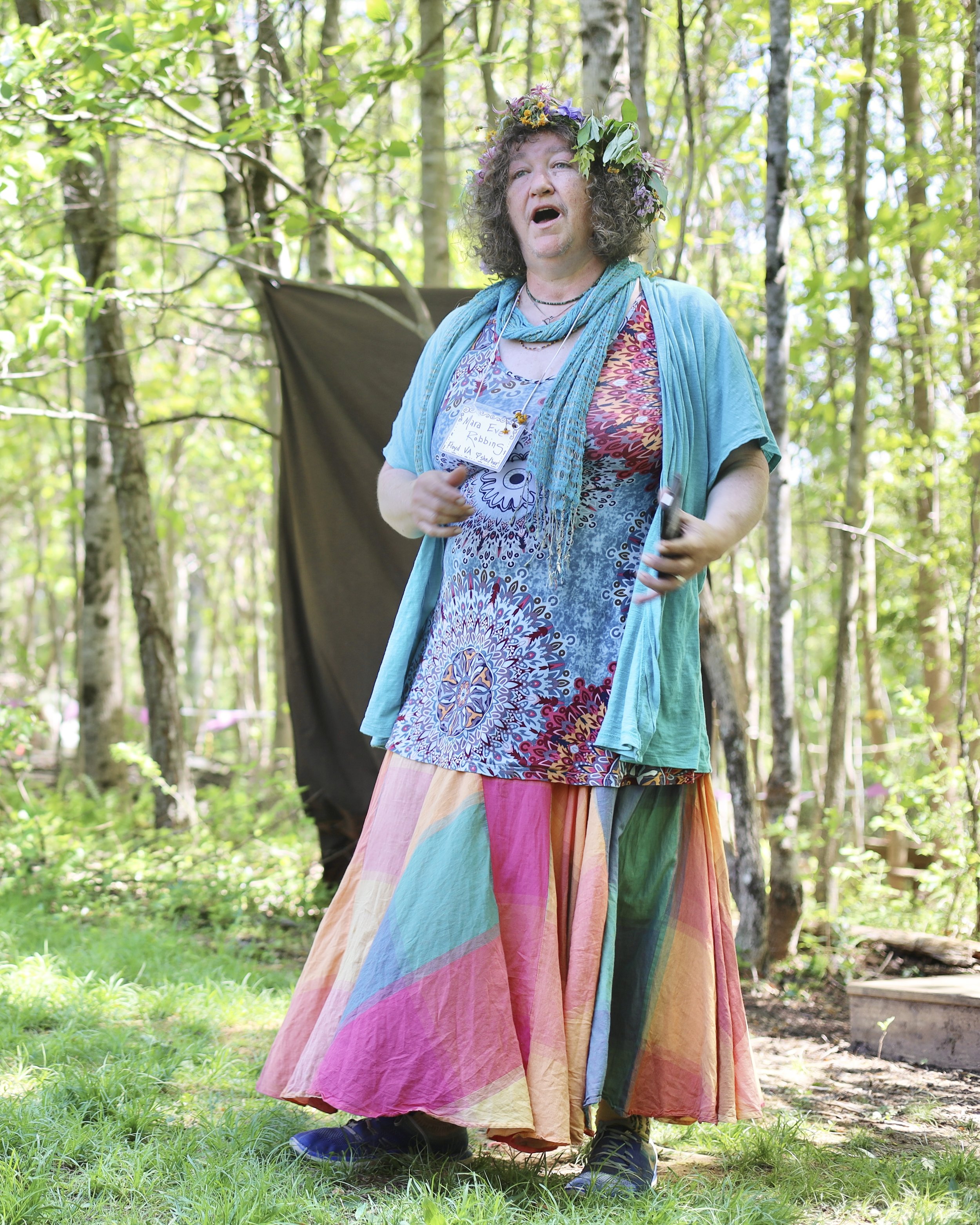 Person in colorful clothing and floral crown outdoors in a forest.