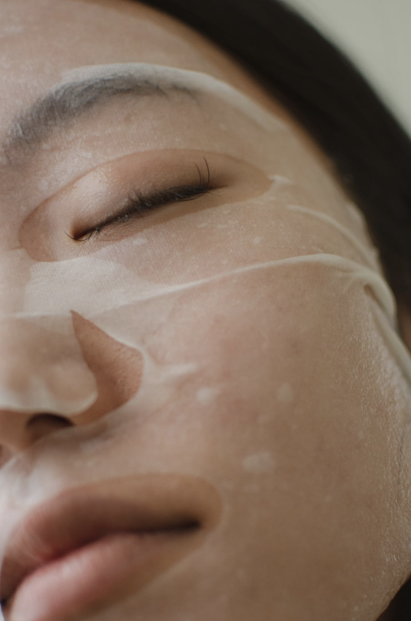 Close up of a dark haired female with a sheet face mask on and eyes closed