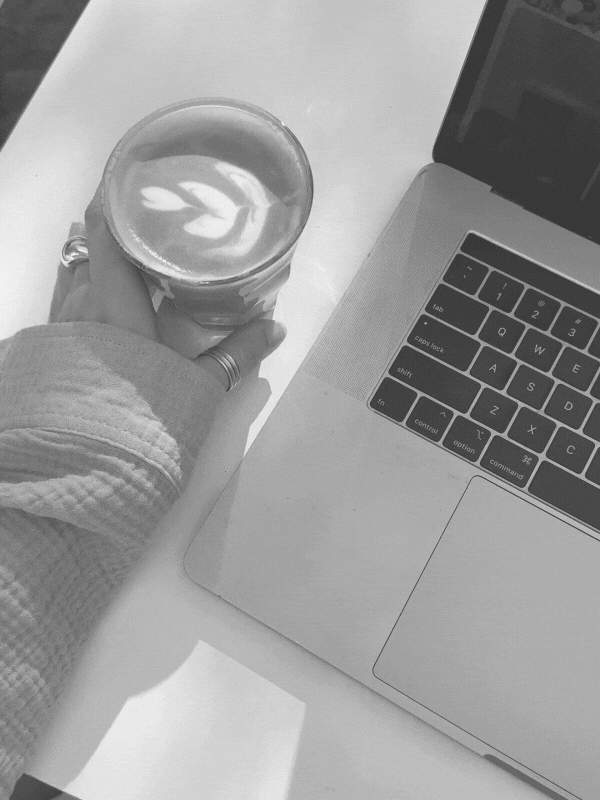 GIF of a hand turning a glass with a latte in it on a table next to a laptop
