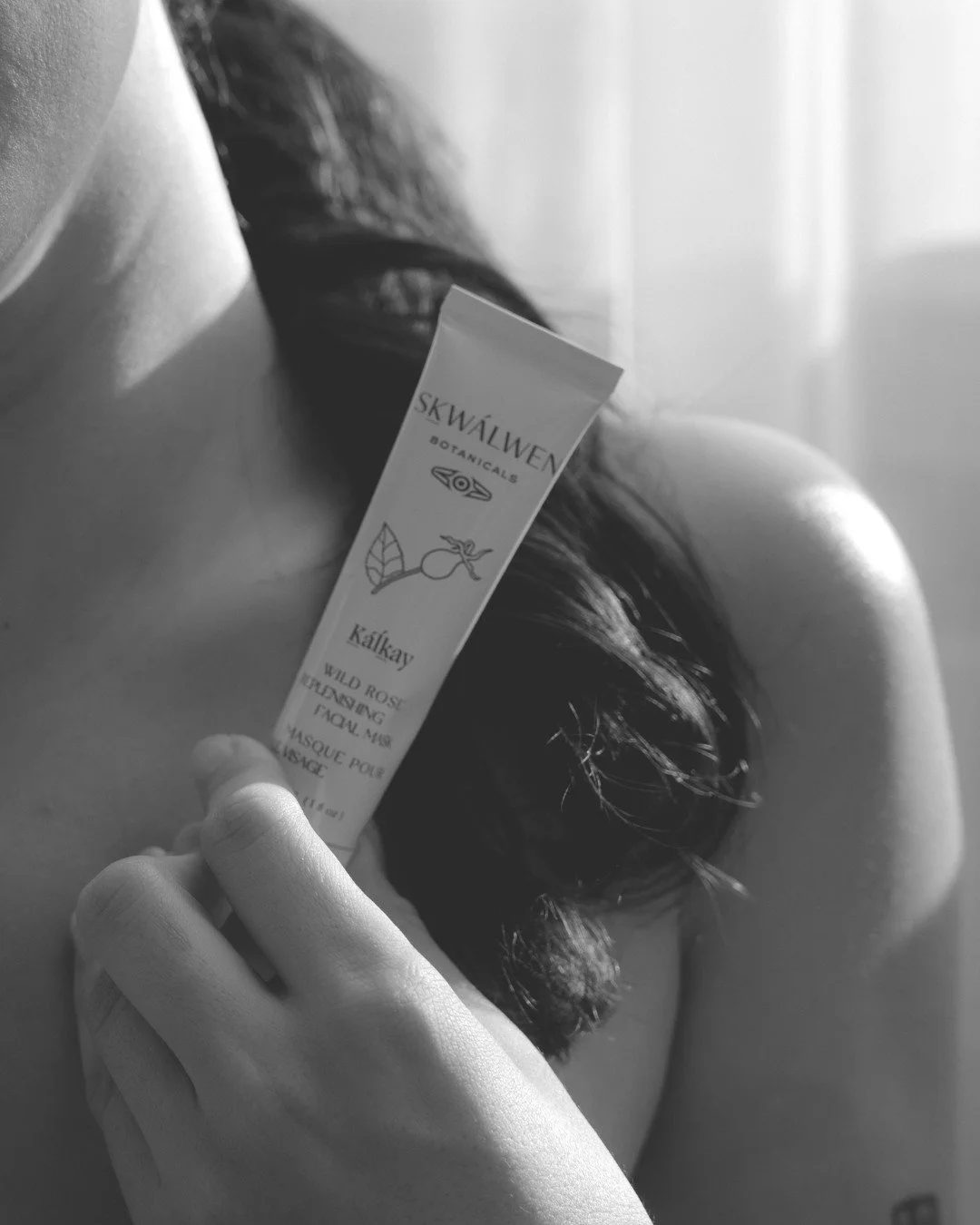 A close up of a Skwalwen Wild Rose Repleneshing Facial Mask tub in the hand of a dark haired female