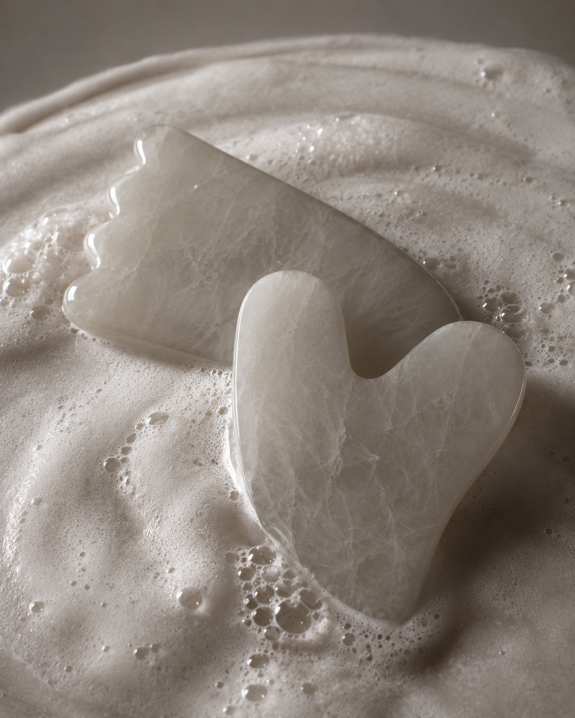 White gua sha tools resting in foamy water