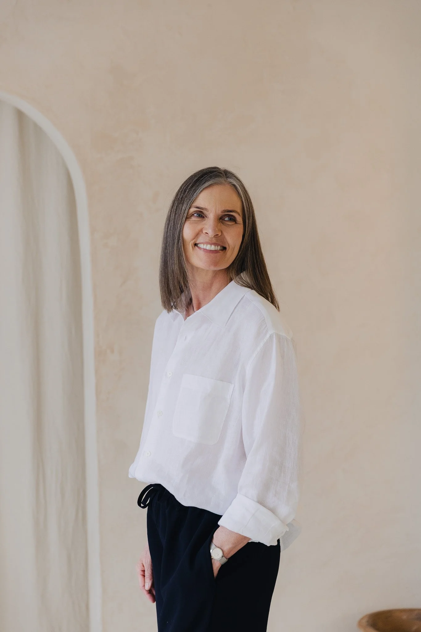Susanne Fjordbach, photographed smiling standing against a neutral wall beside an arched doorway