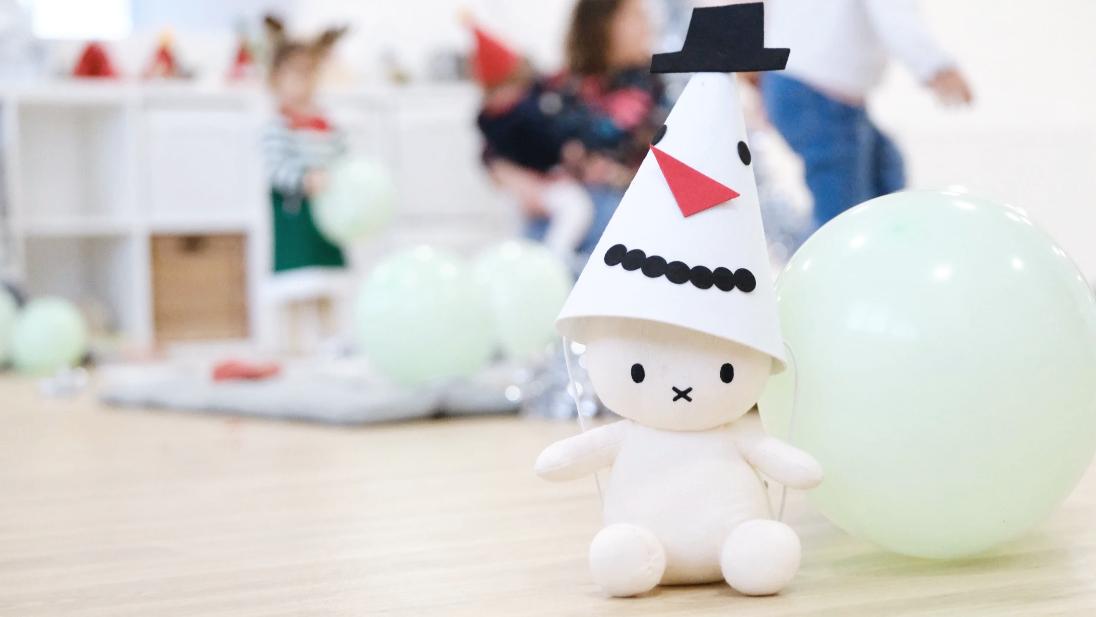 white bunny toy wearing a snow man hat with children playing in the background