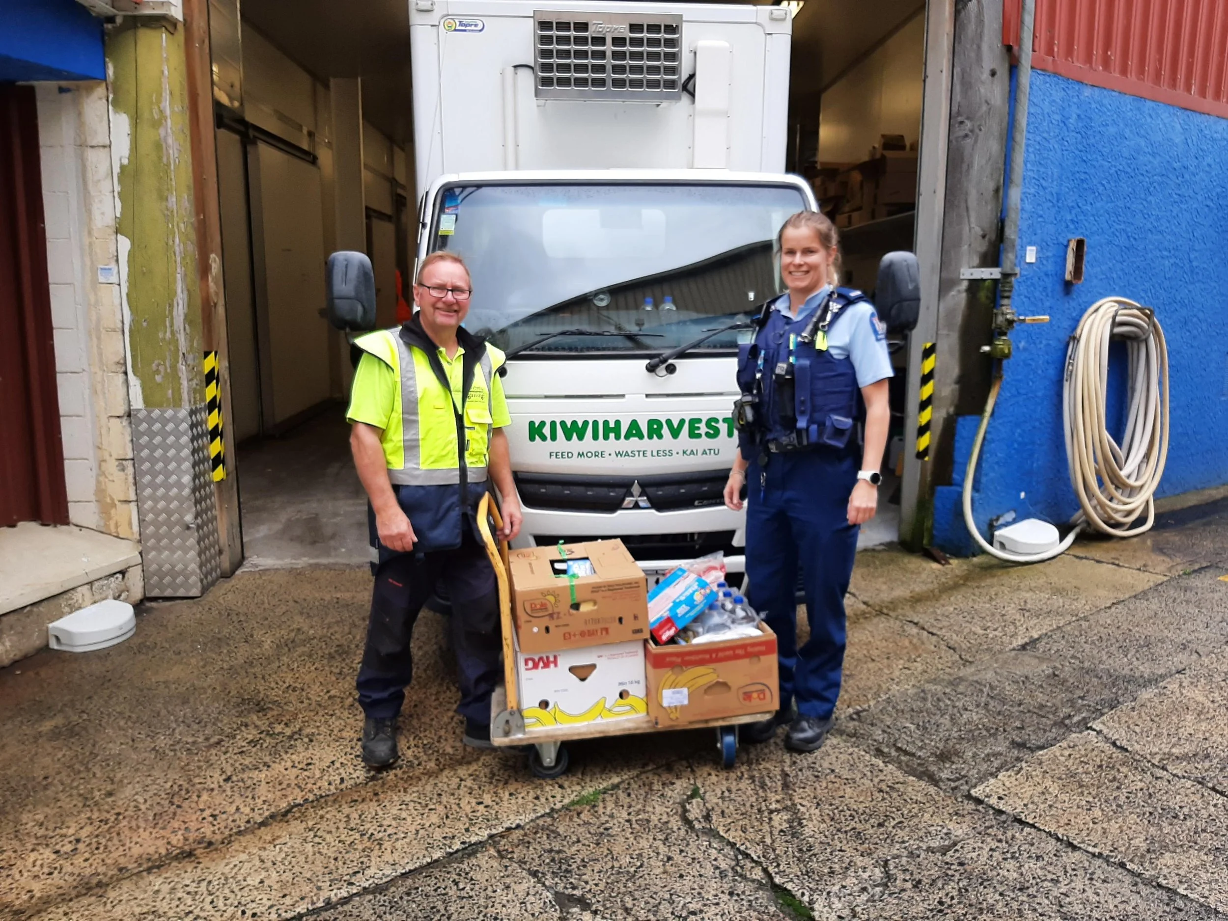 KiwiHarvest Dunedin Warehouse supervisor stands infront of the KiwiHarvest food rescue truck with a police officer and a few boxes of donated food