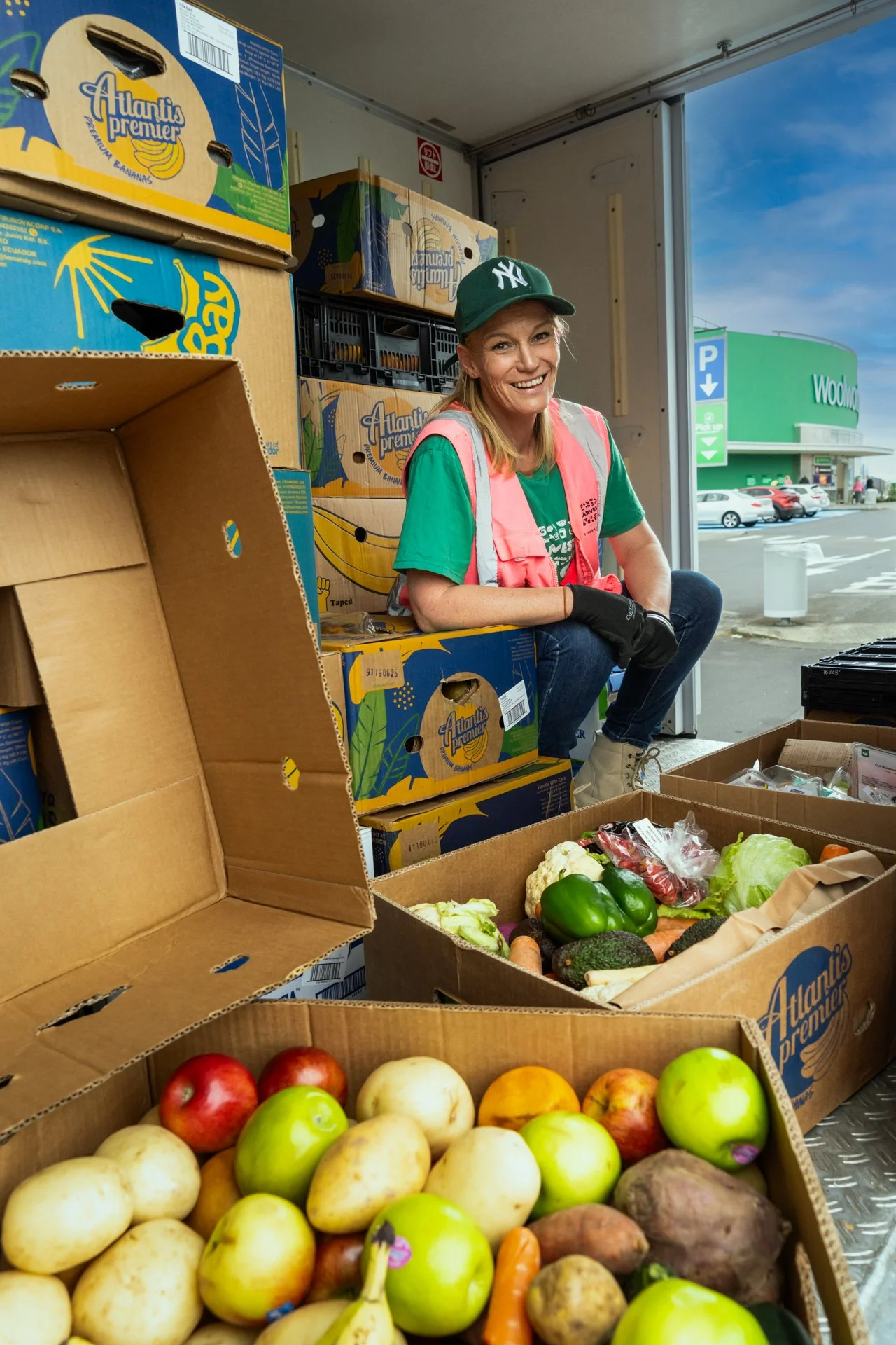 KiwiHarvest food rescue driver sits in the back of the KiwiHarvest food rescue van, around the driver are boxes for fresh fruits and vegetables