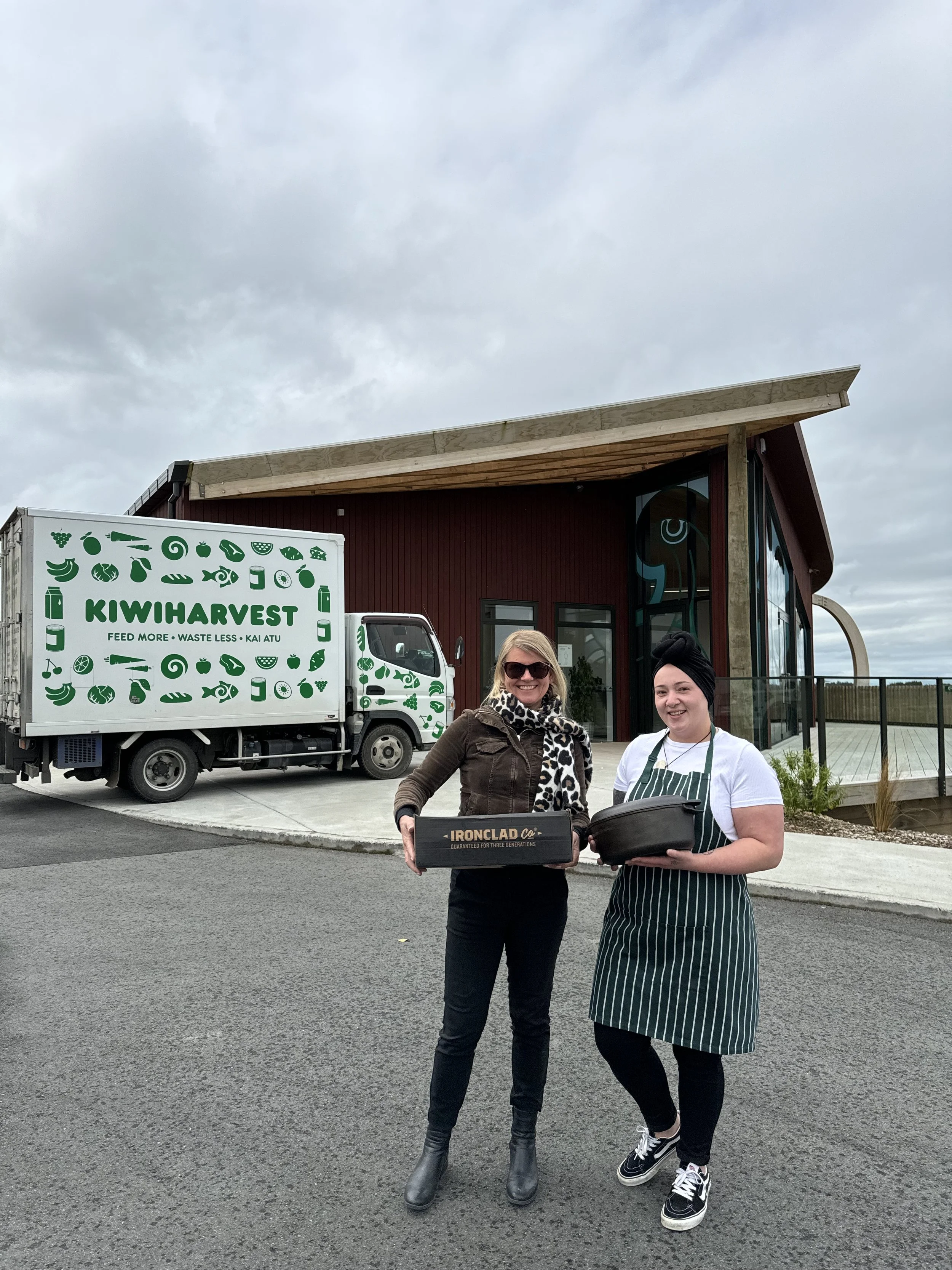 KiwiHarvest relationship manager stands outside with a chef, holding an irion clad pan co dutch oven. The KiwiHarvest food truck is in the background