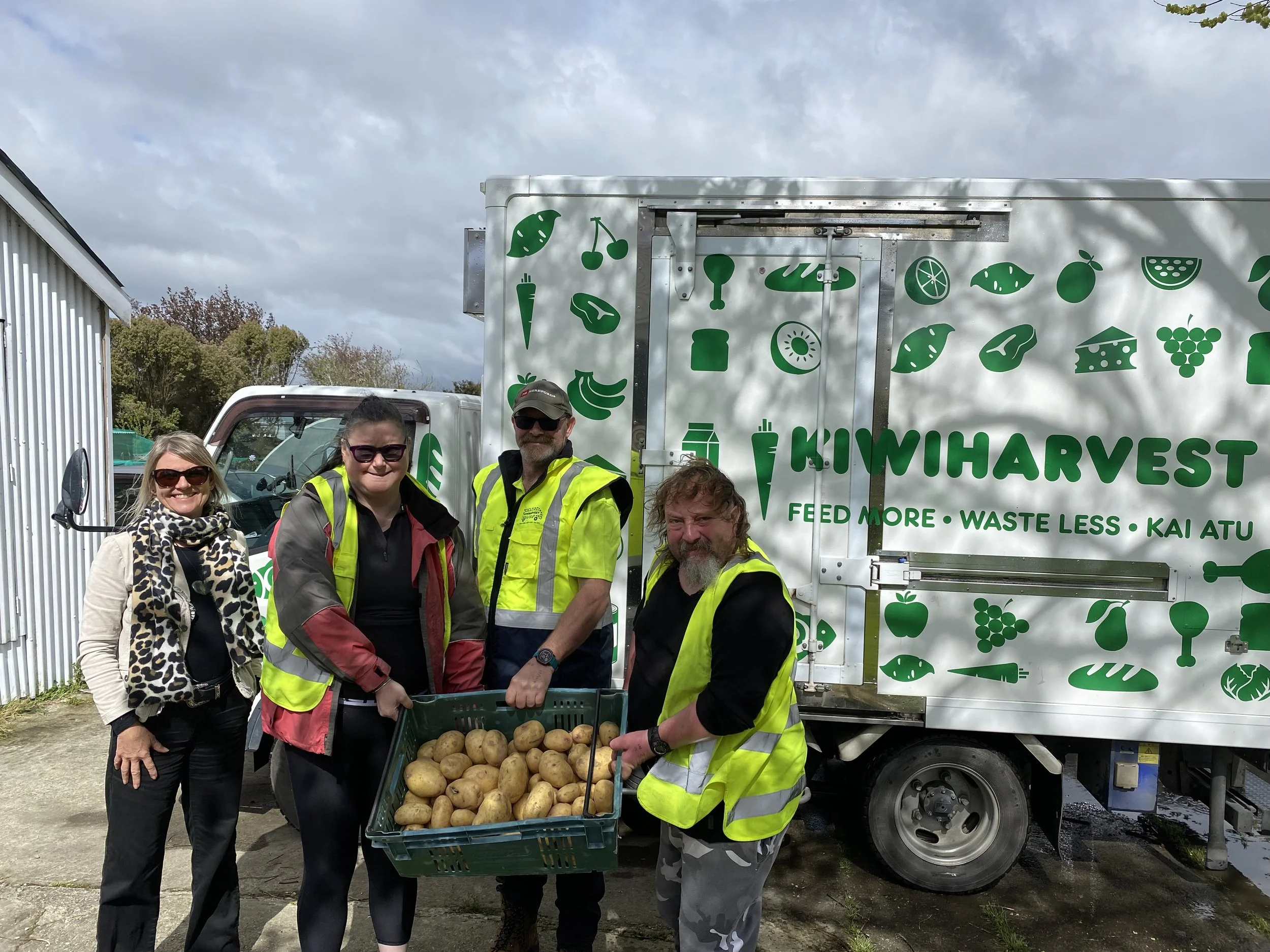 KiwiHarvest relationship manager and KiwiHarvest food rescue driver stands with two team members from a charitable partner, together they are holding a crate of donated potatoes