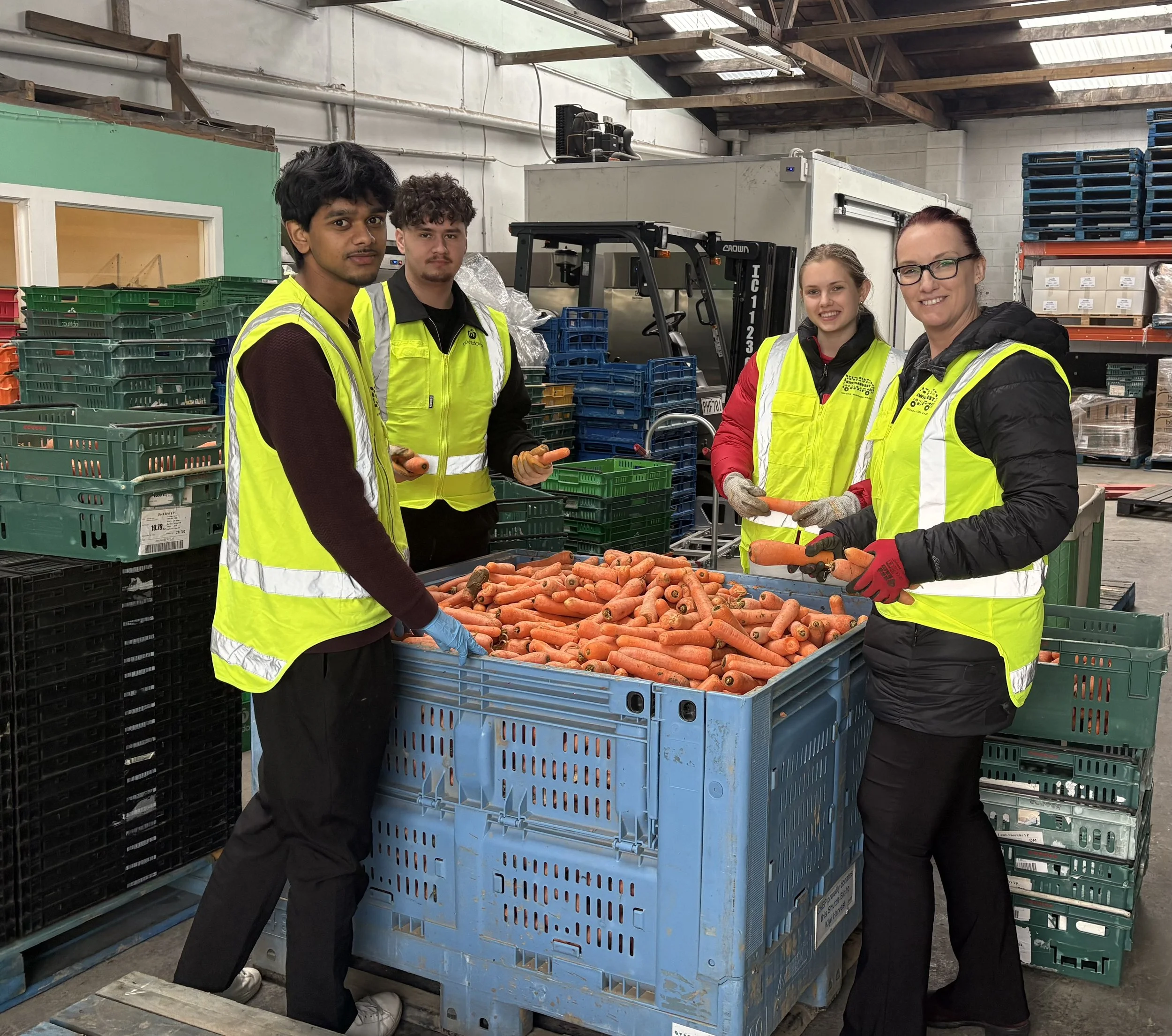 volunteers stand round a create of carrots smiling